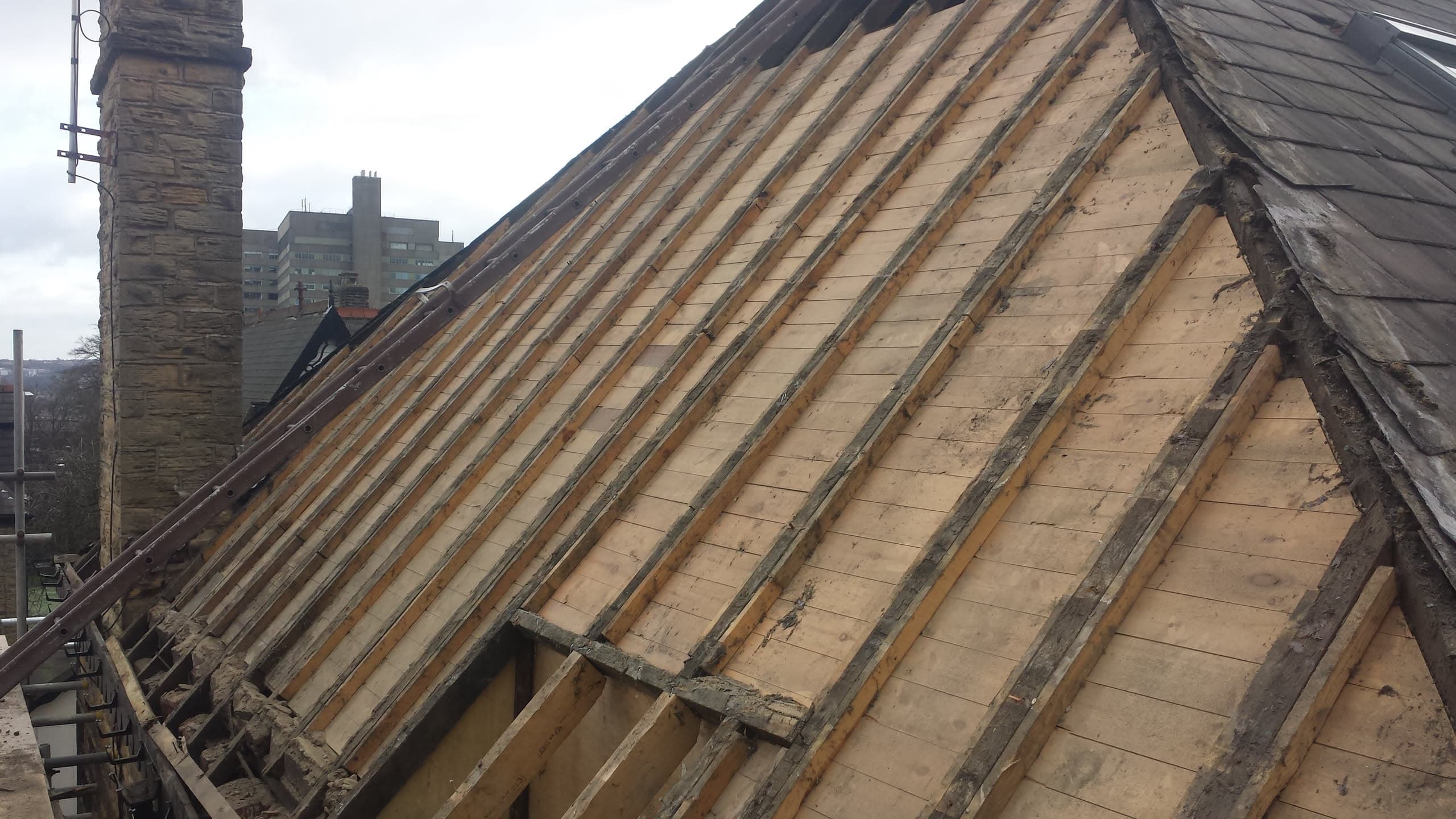 Pitched roof stripped to timber battens during re-roofing work with chimney stack visible
