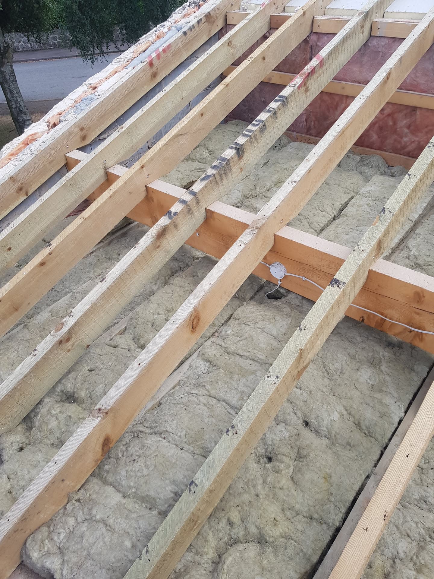 Pitched roof structure with timber rafters and insulation between joists during construction