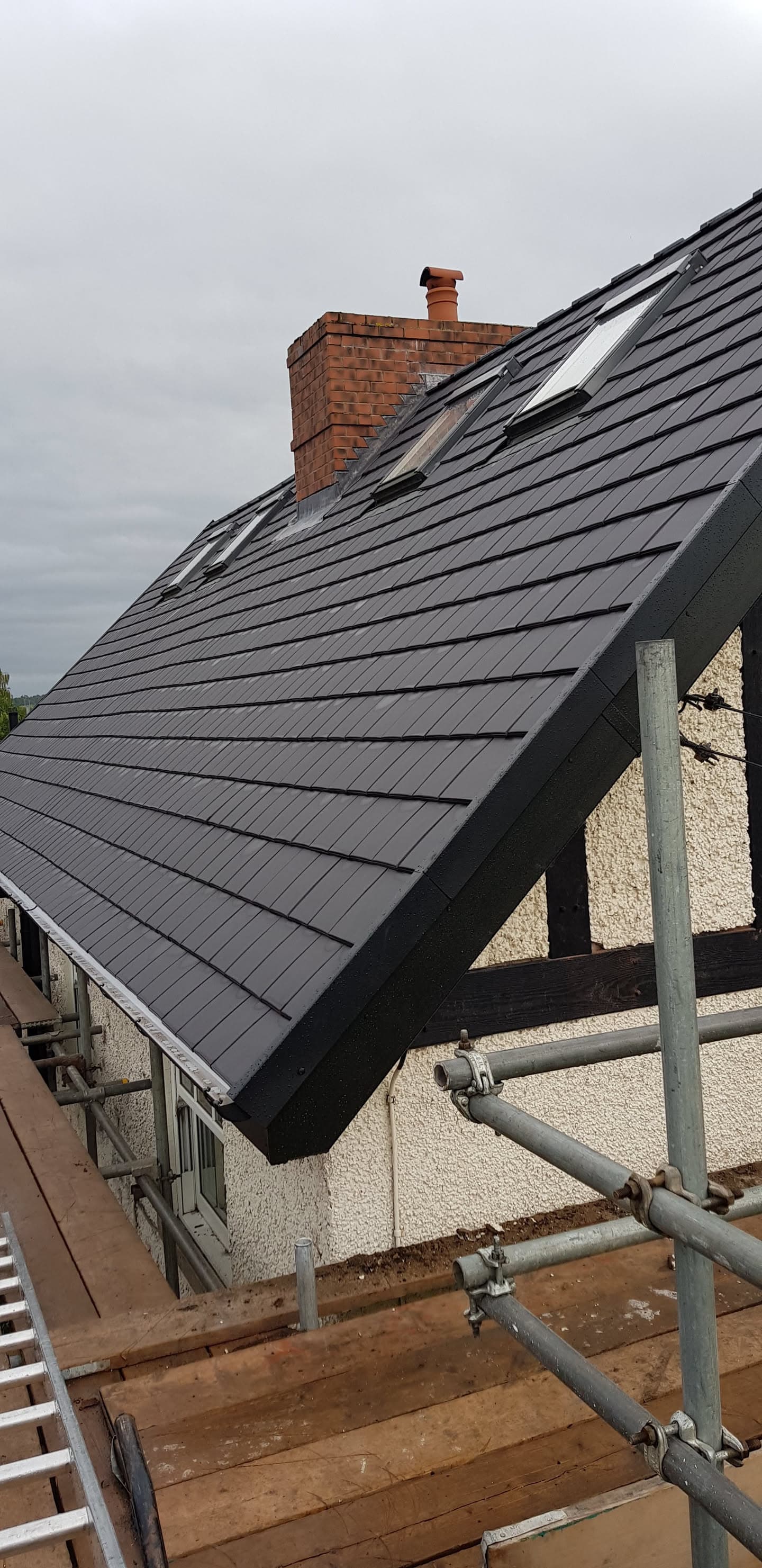 Pitched roof with dark grey slate tiles, brick chimney stack and scaffolding