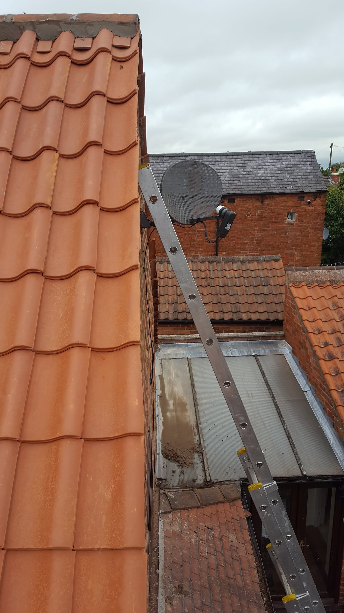 Orange concrete tiled pitched roof with ladder and flat roof extension visible below