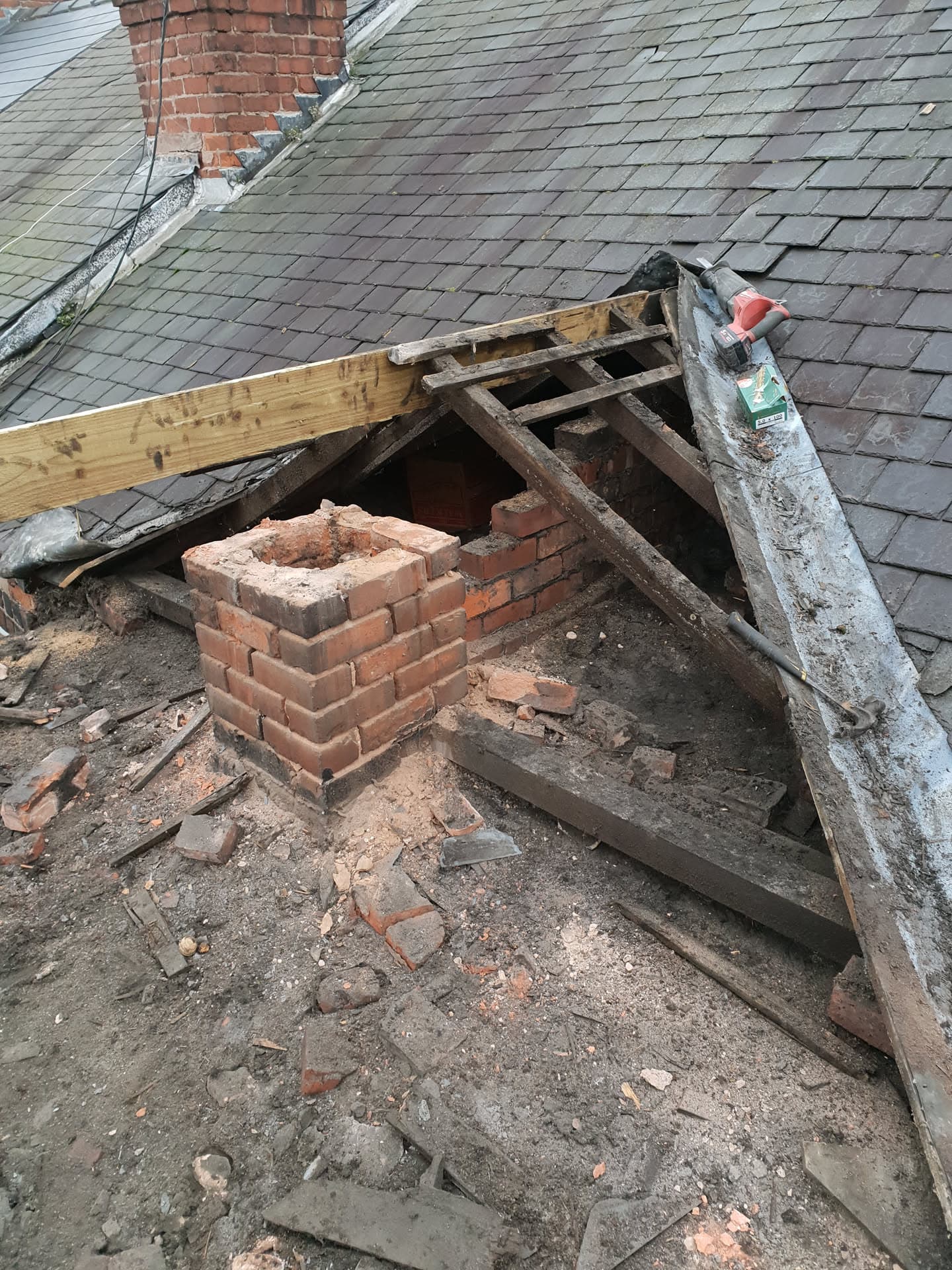Pitched slate roof with exposed chimney stack and timber framework during repair work