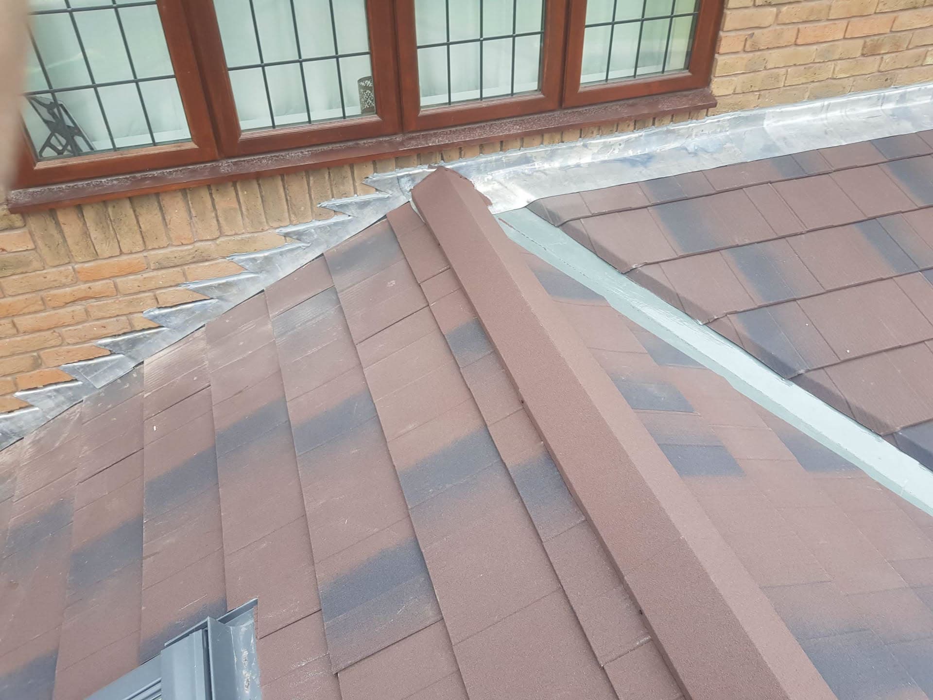 Pitched roof with brown concrete tiles, lead flashing and ridge detail against conservatory windows