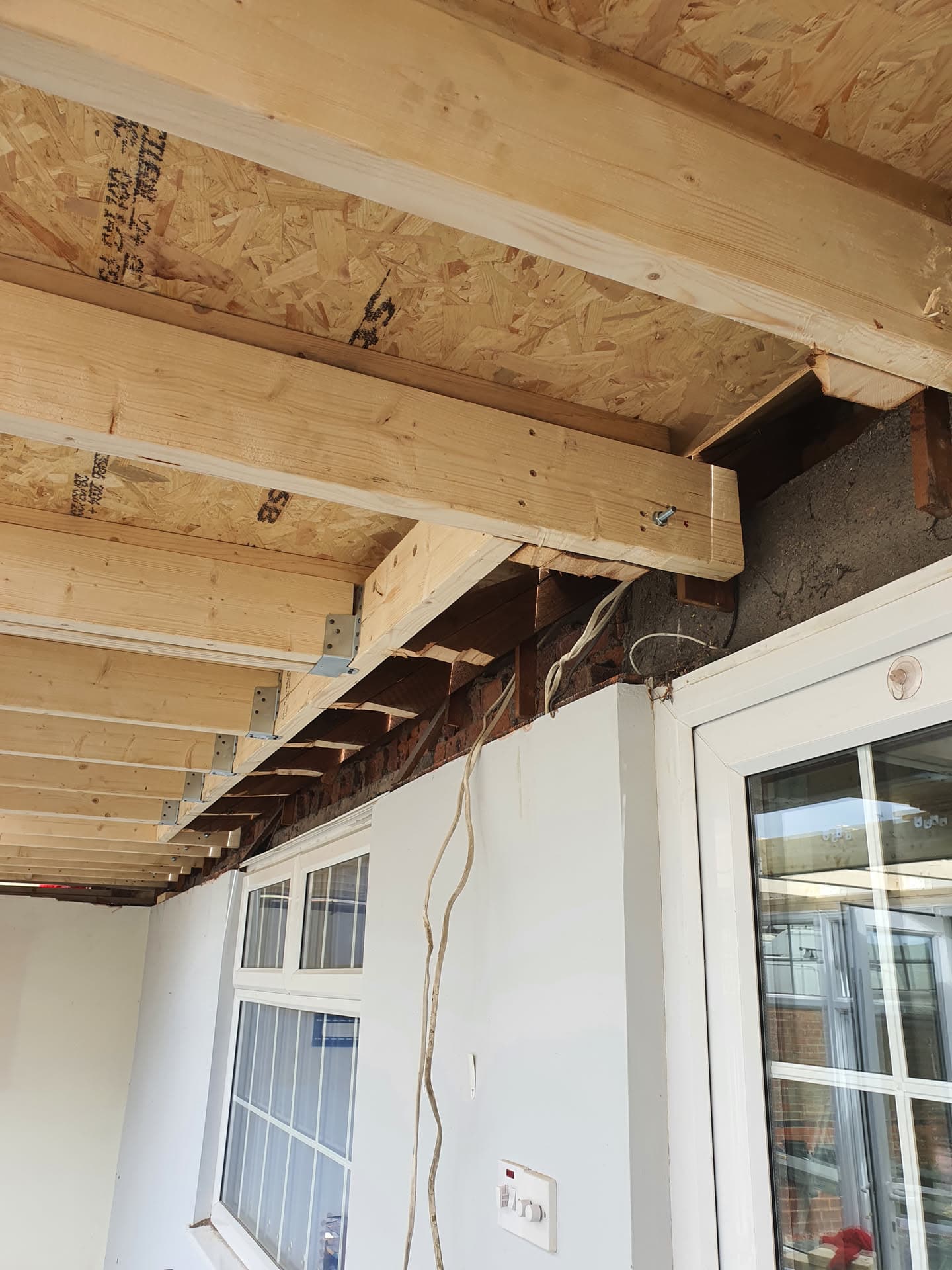 Exposed timber joists and OSB decking during flat roof construction above conservatory