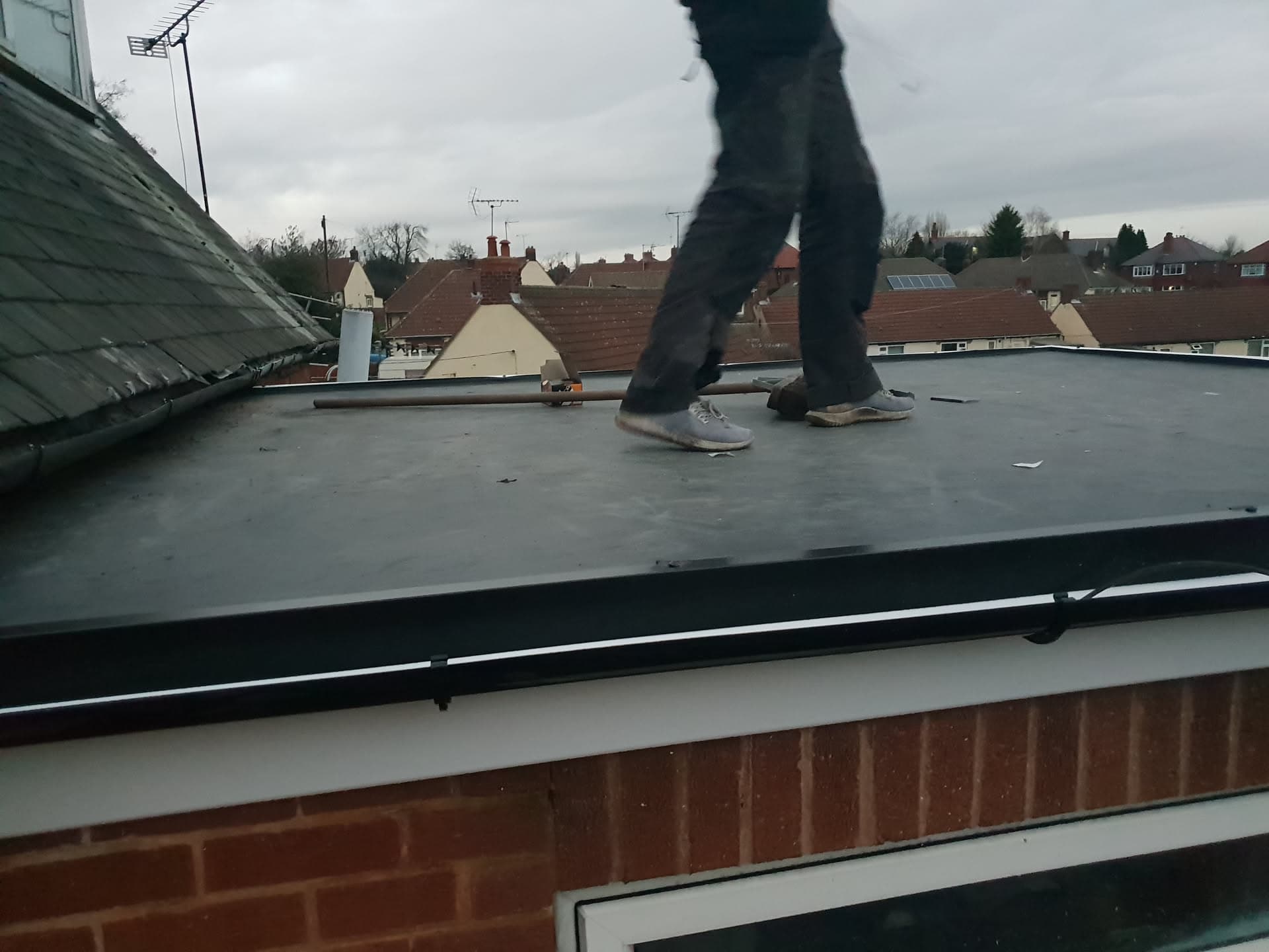 Fitter working on flat roof with EPDM rubber membrane and white fascia trim