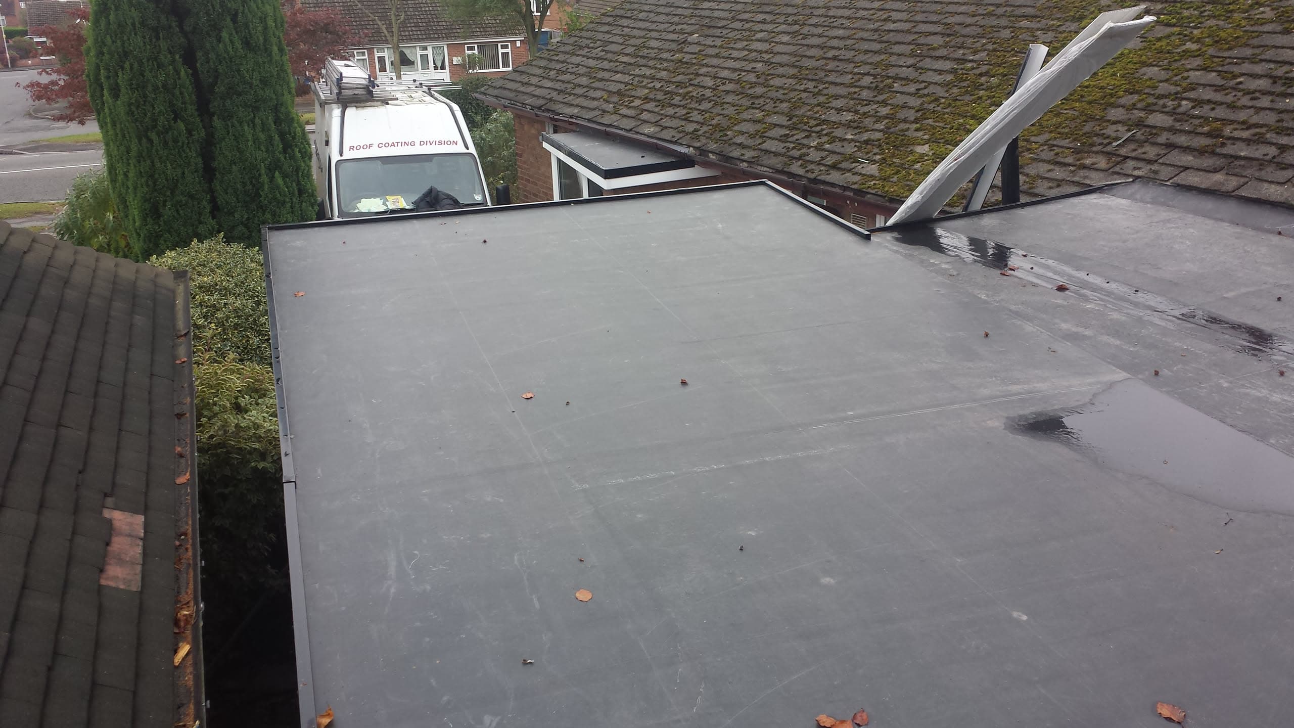 Grey flat roof with EPDM rubber membrane on residential extension, adjacent tiled pitched roofs visible