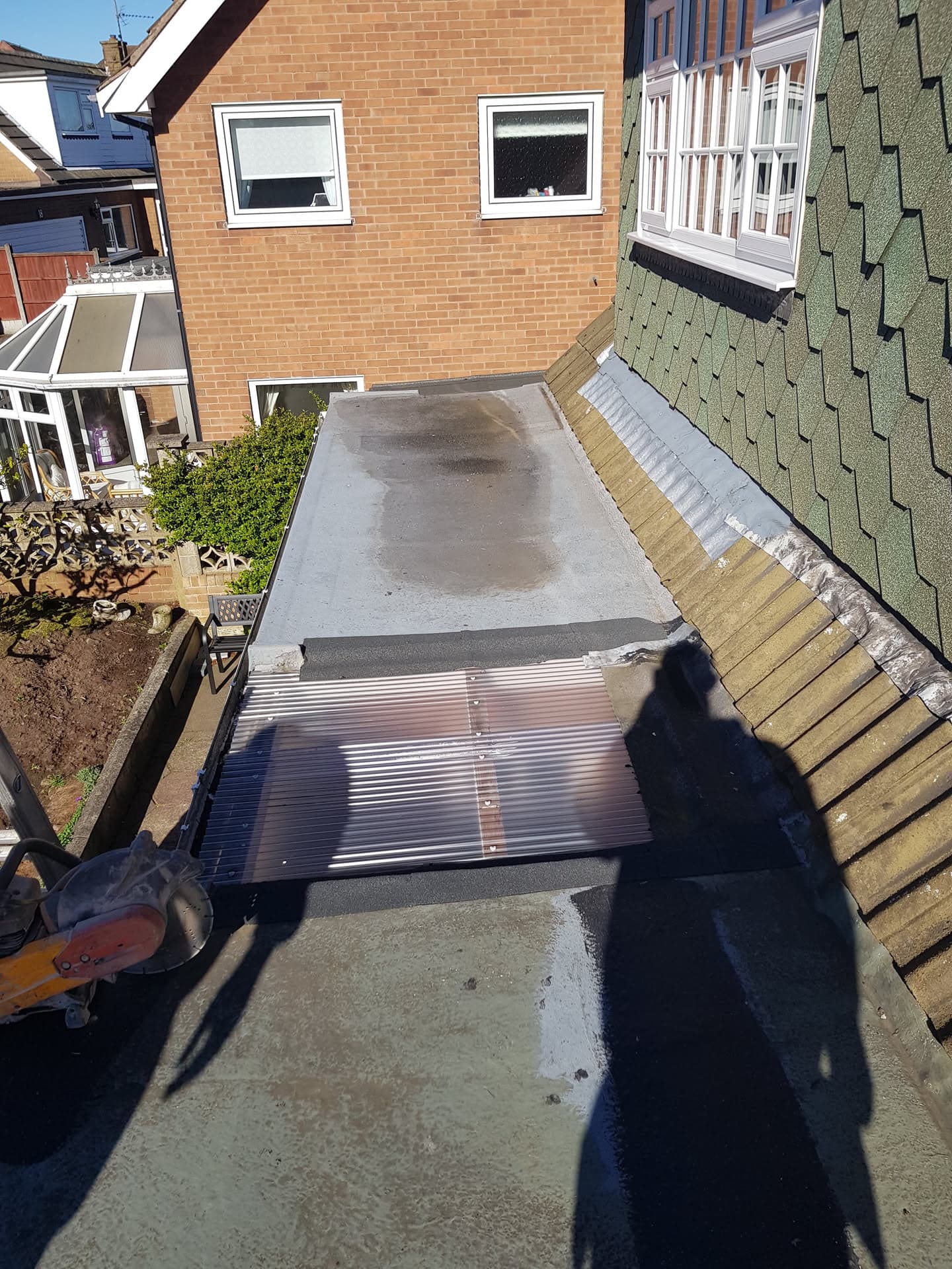 Flat roof extension with GRP fibreglass finish and corrugated metal roofing section adjoining tiled pitched roof