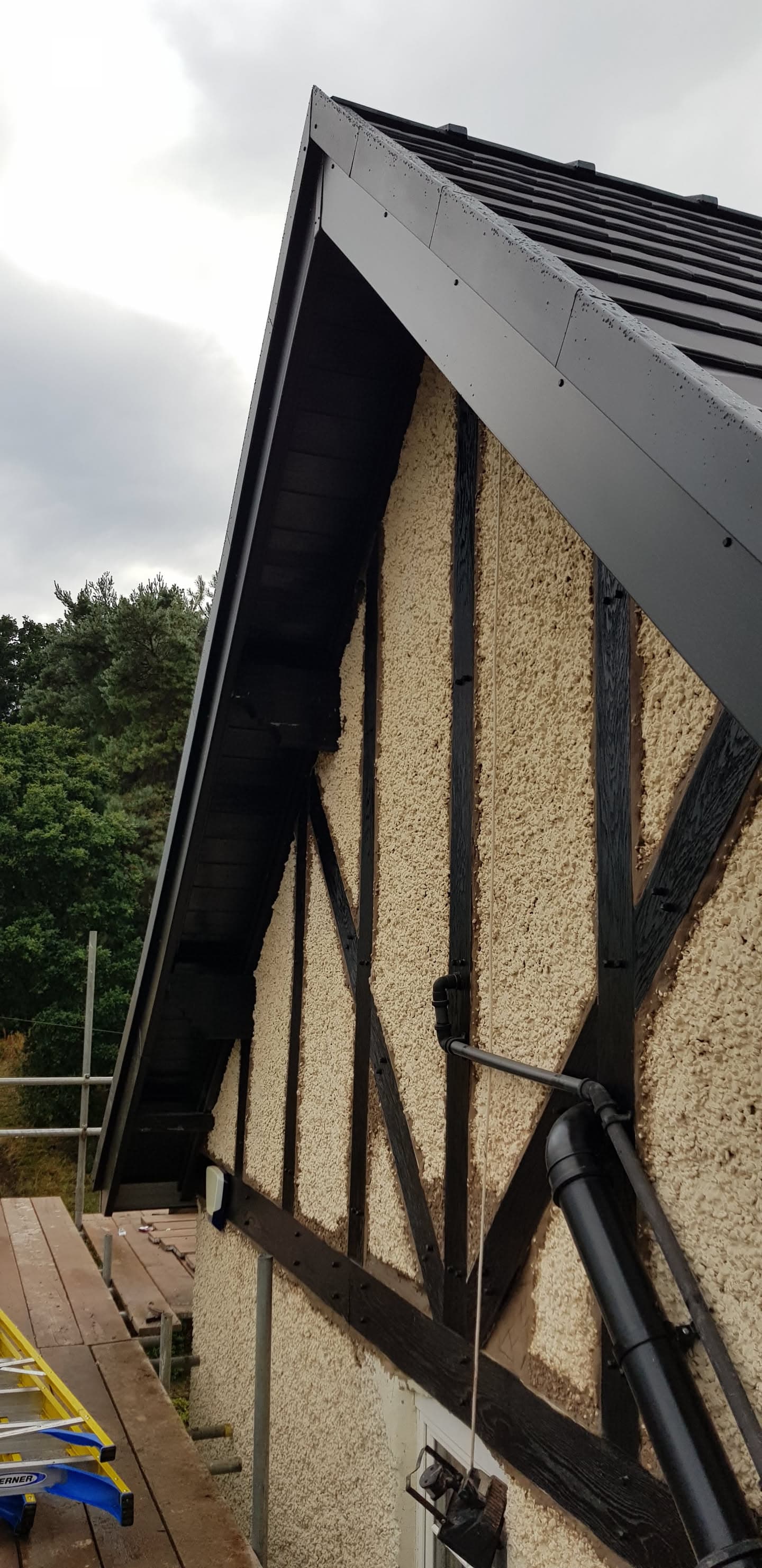 Pitched roof with dark tiled finish, white fascia boards and black guttering on timber-framed gable