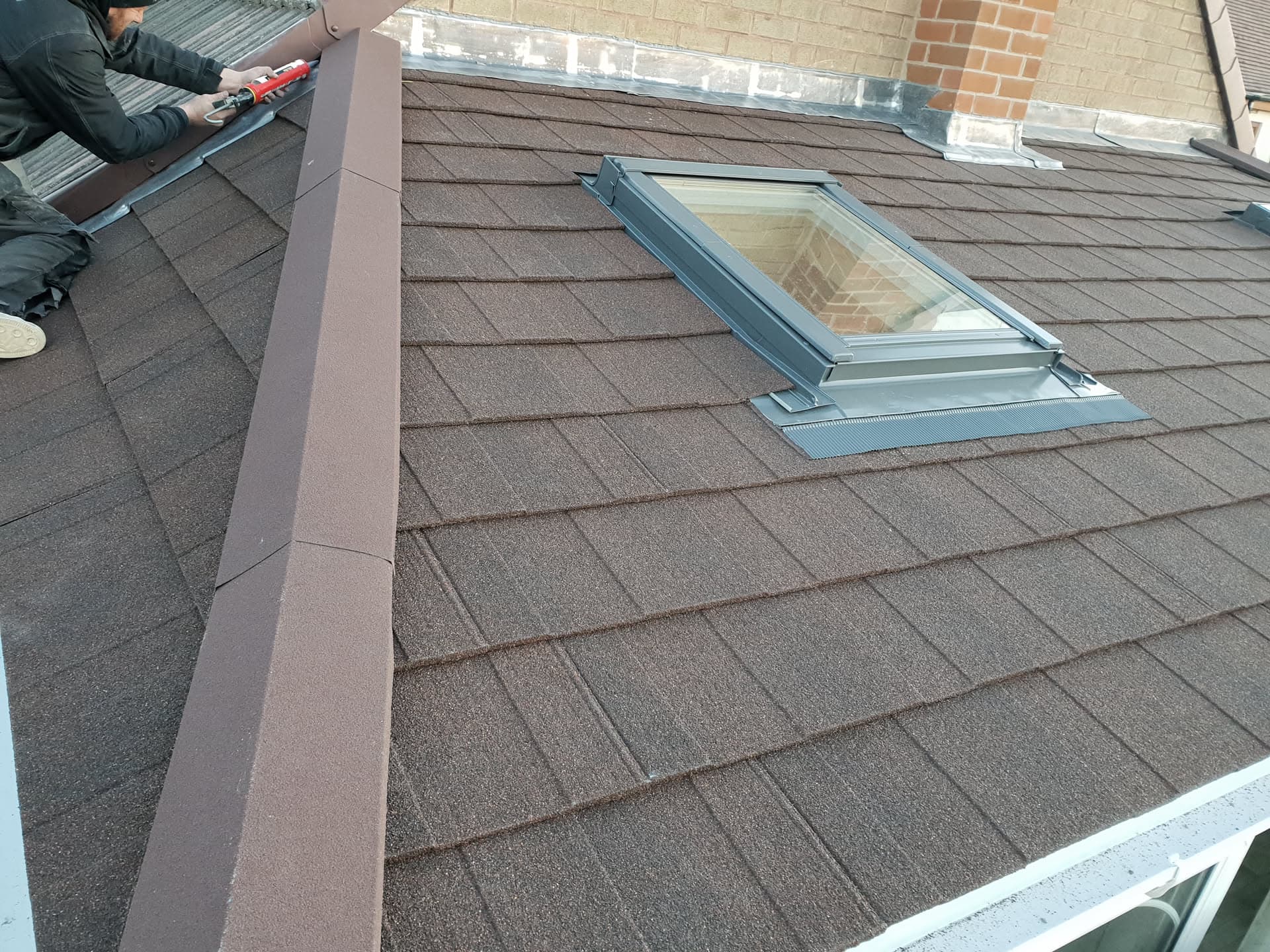 Fitter installing brown concrete tiled pitched roof with skylight window and fascia boards