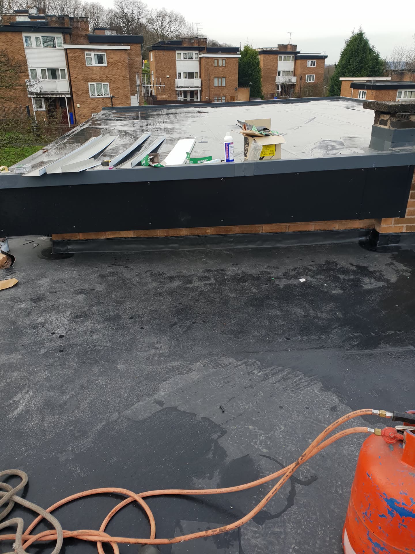 Flat roof installation in progress with felt membrane and dark fascia boards