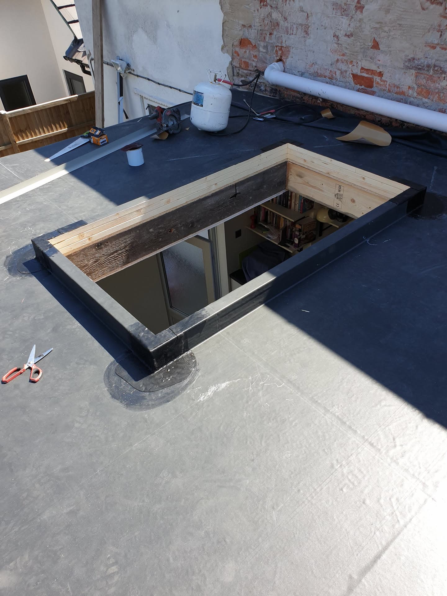 Flat roof with dark grey rubber membrane and timber-framed skylight opening