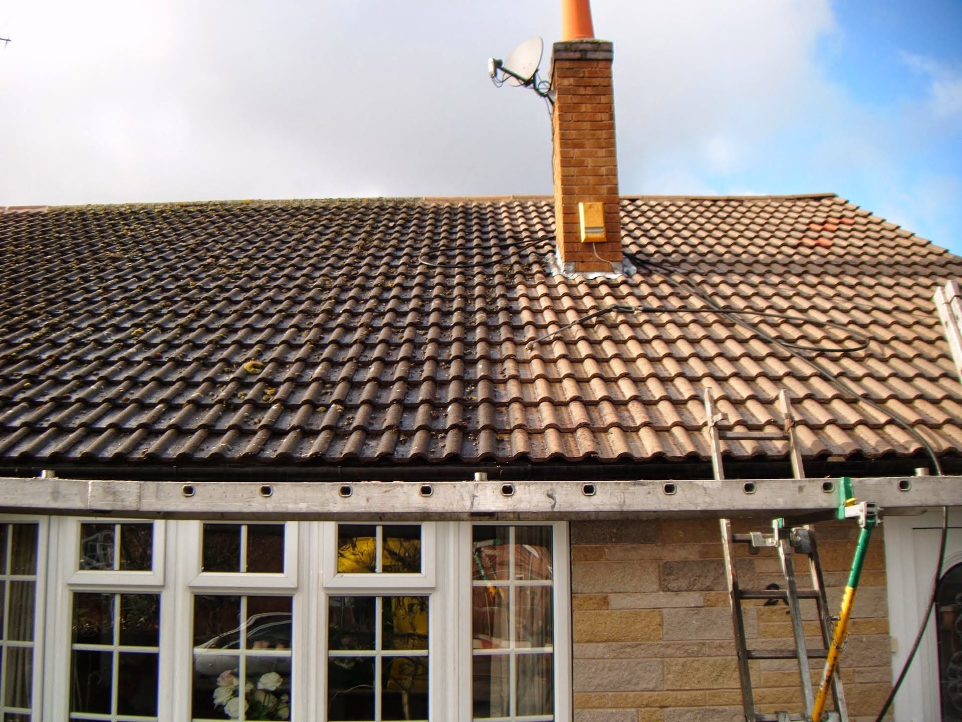 Pitched roof with brown concrete tiles, brick chimney stack and fascia board