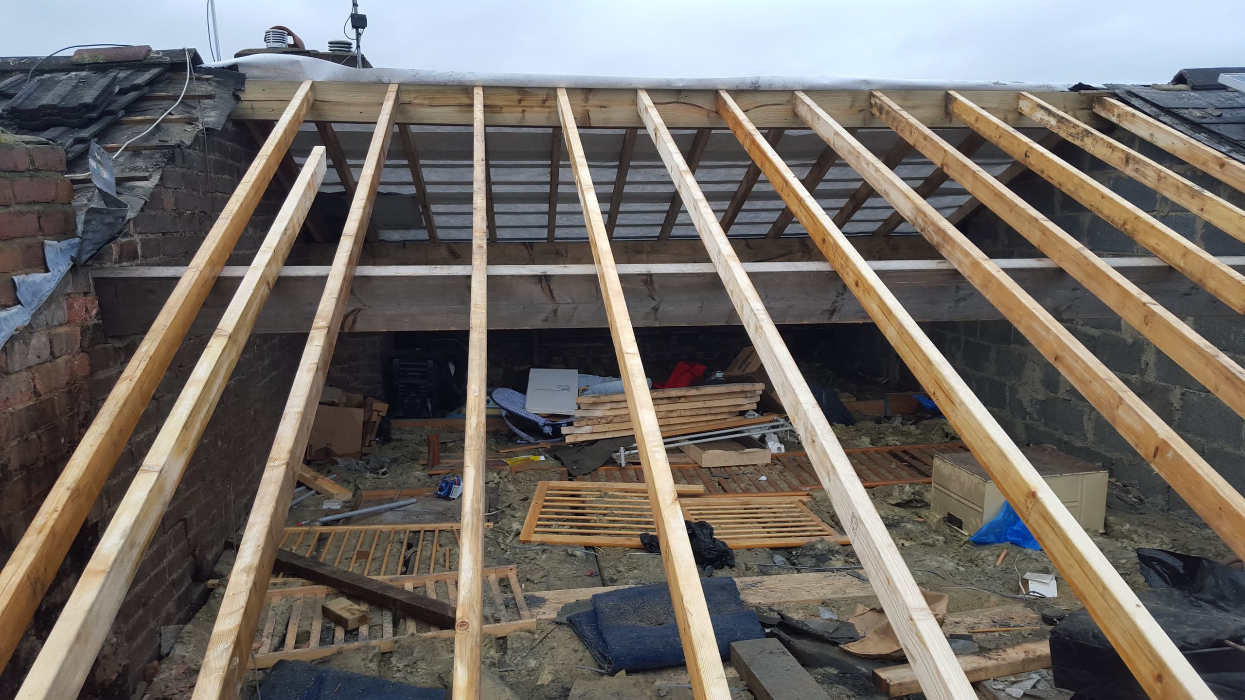 Pitched roof under construction showing exposed timber rafters and joists before covering