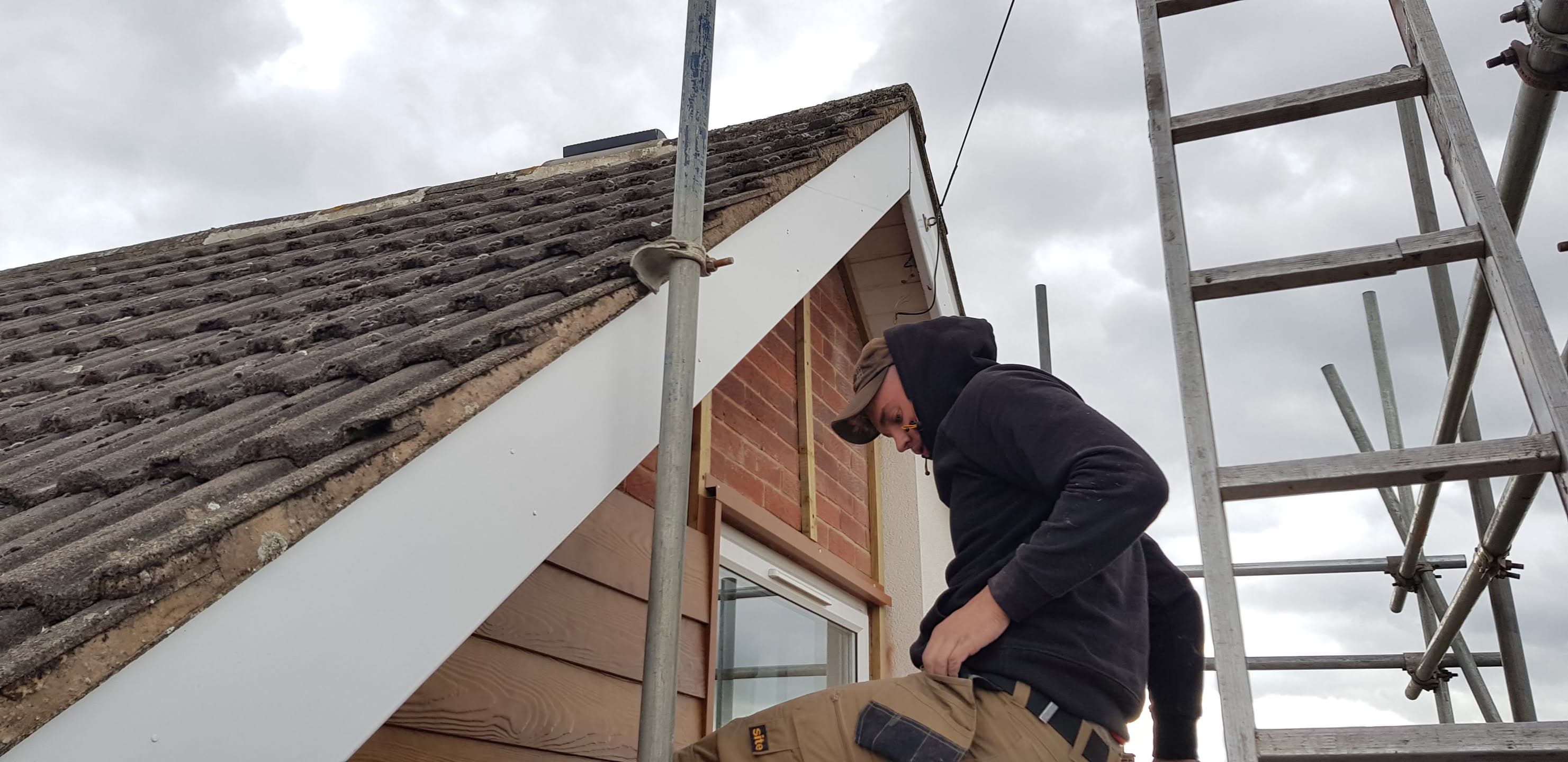 Fitter installing fascia boards on pitched roof with concrete tiles and scaffolding