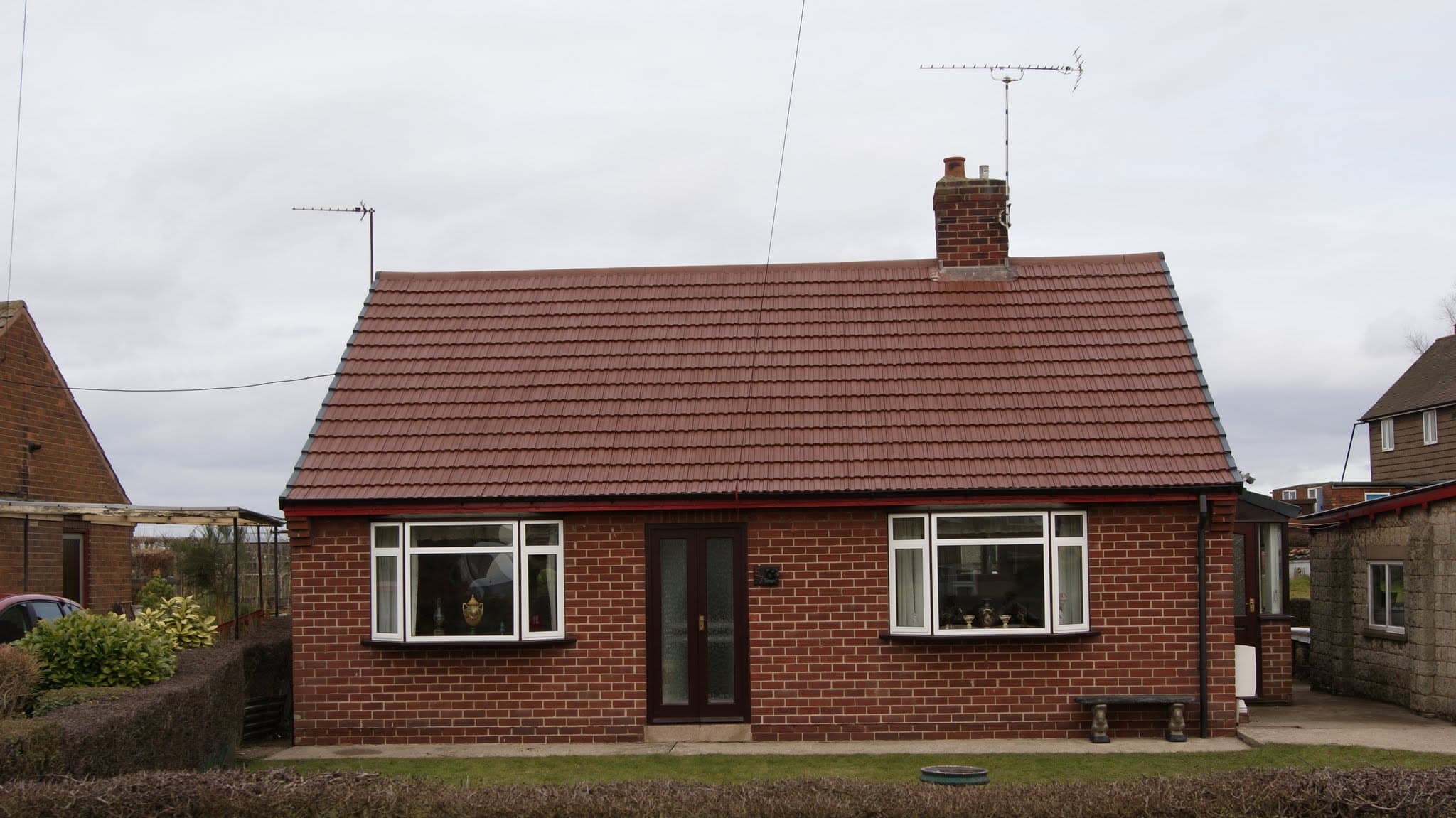Red brick bungalow with brown concrete tiled pitched roof and chimney stack