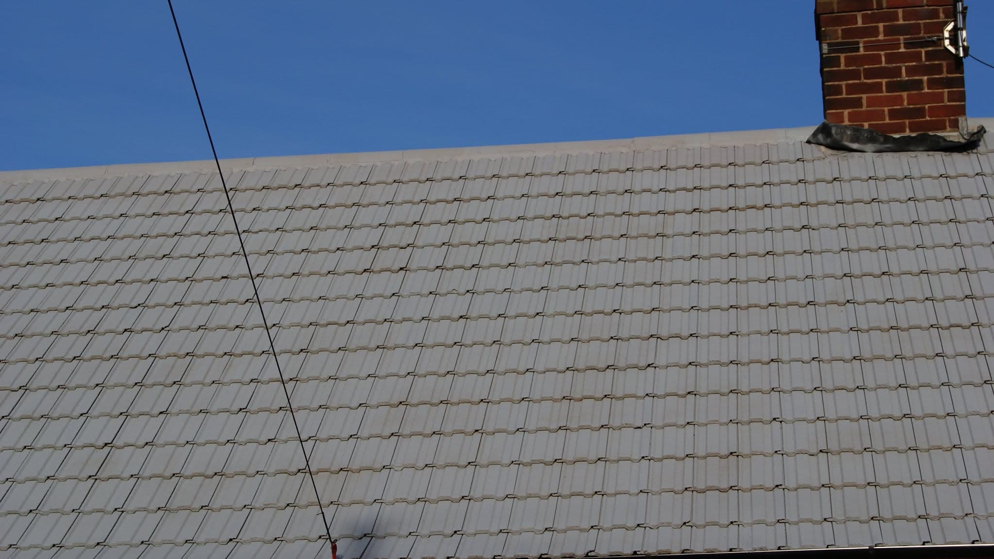 Pitched roof with grey concrete tiles and brick chimney stack