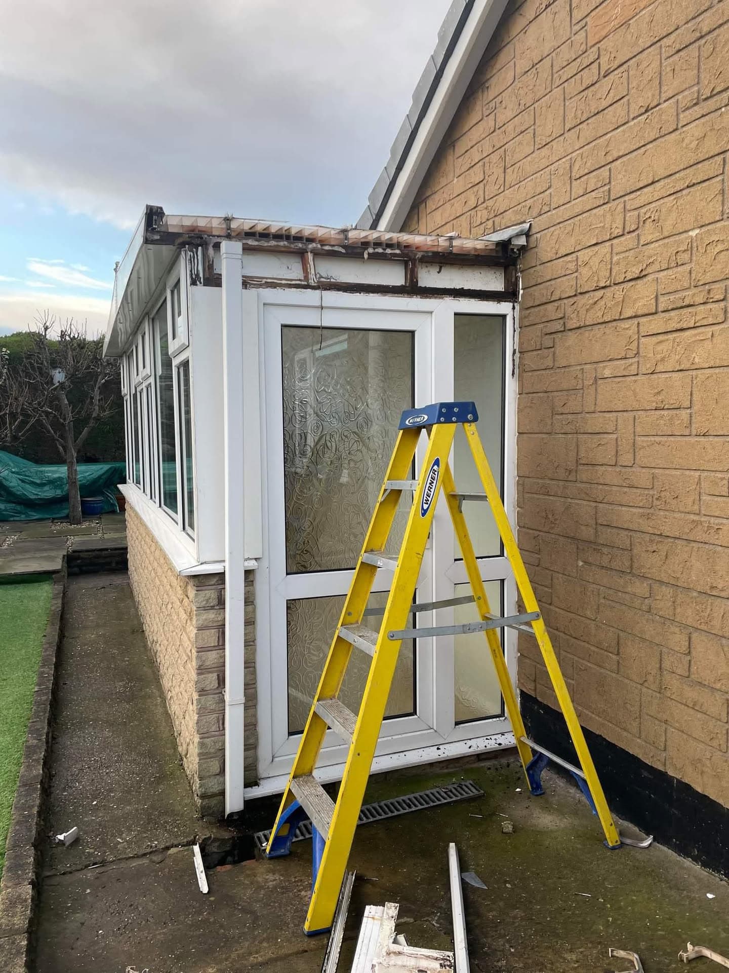 Conservatory roof replacement in progress with damaged felt roof and white uPVC frames