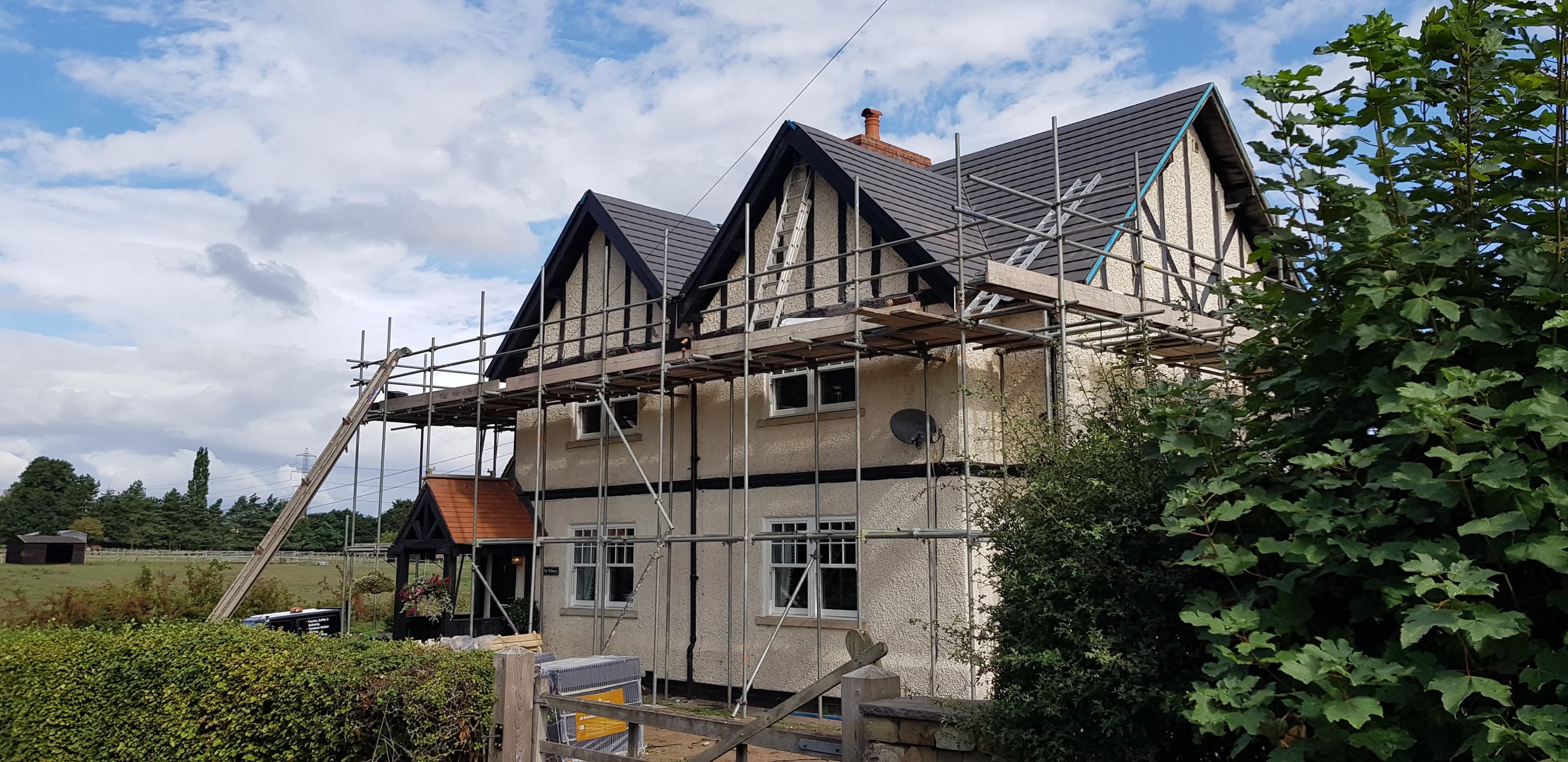 Pitched roof with dark grey tiles and scaffolding during roofing work
