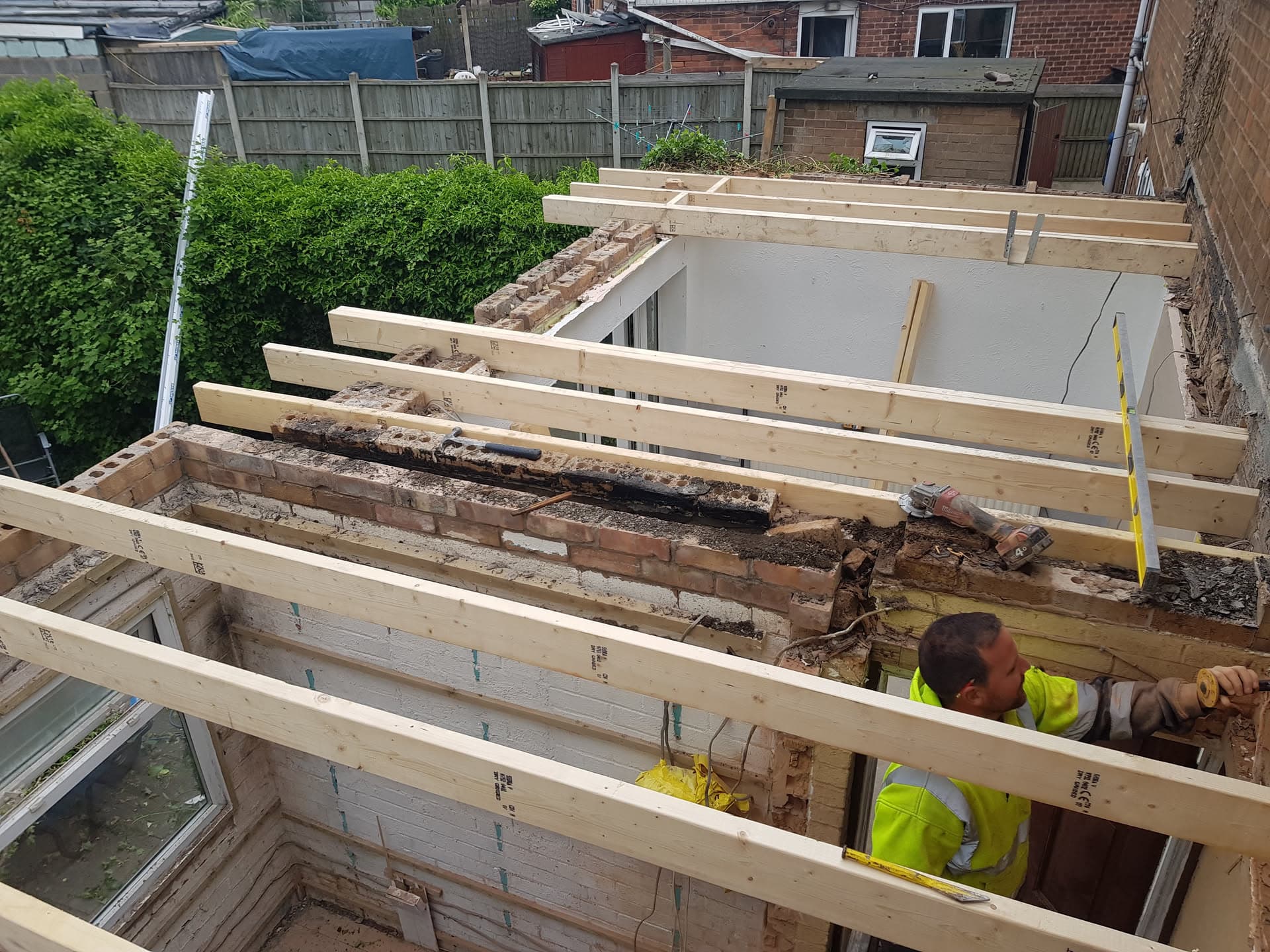 Flat roof replacement in progress with new timber joists being installed by fitters in high-visibility clothing