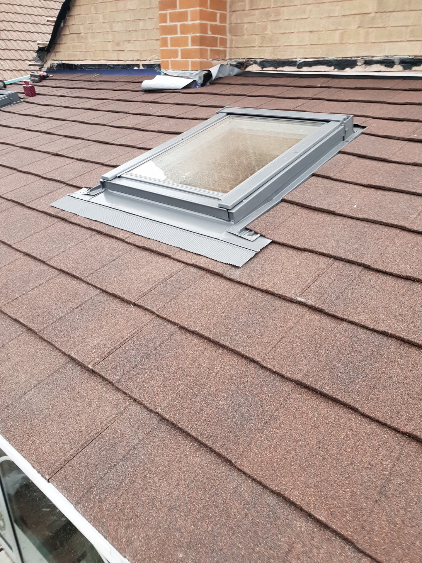 Pitched roof with brown concrete tiles and newly installed roof window with grey flashing