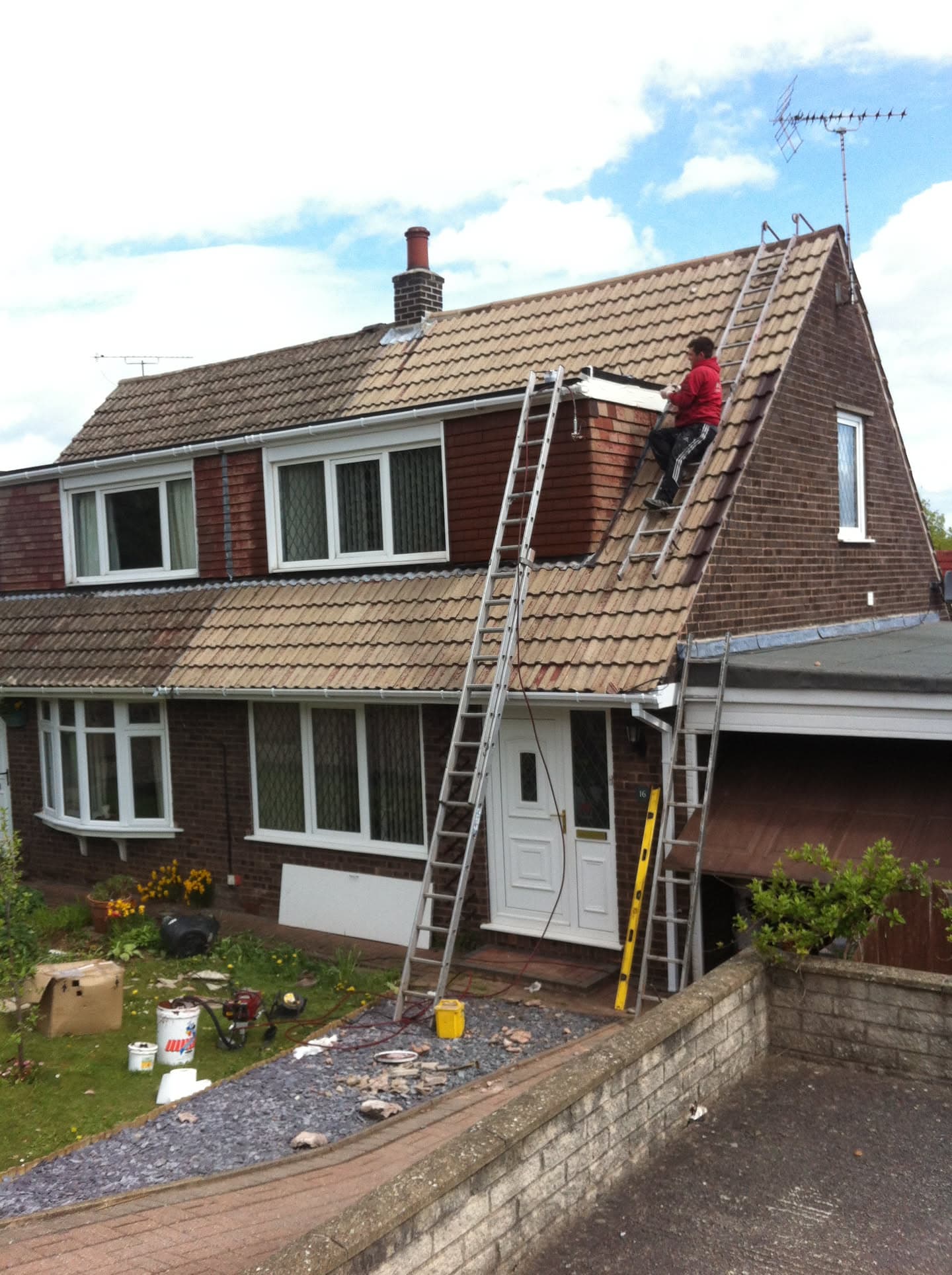 Fitter working on pitched concrete tiled roof with ladder access and chimney stack