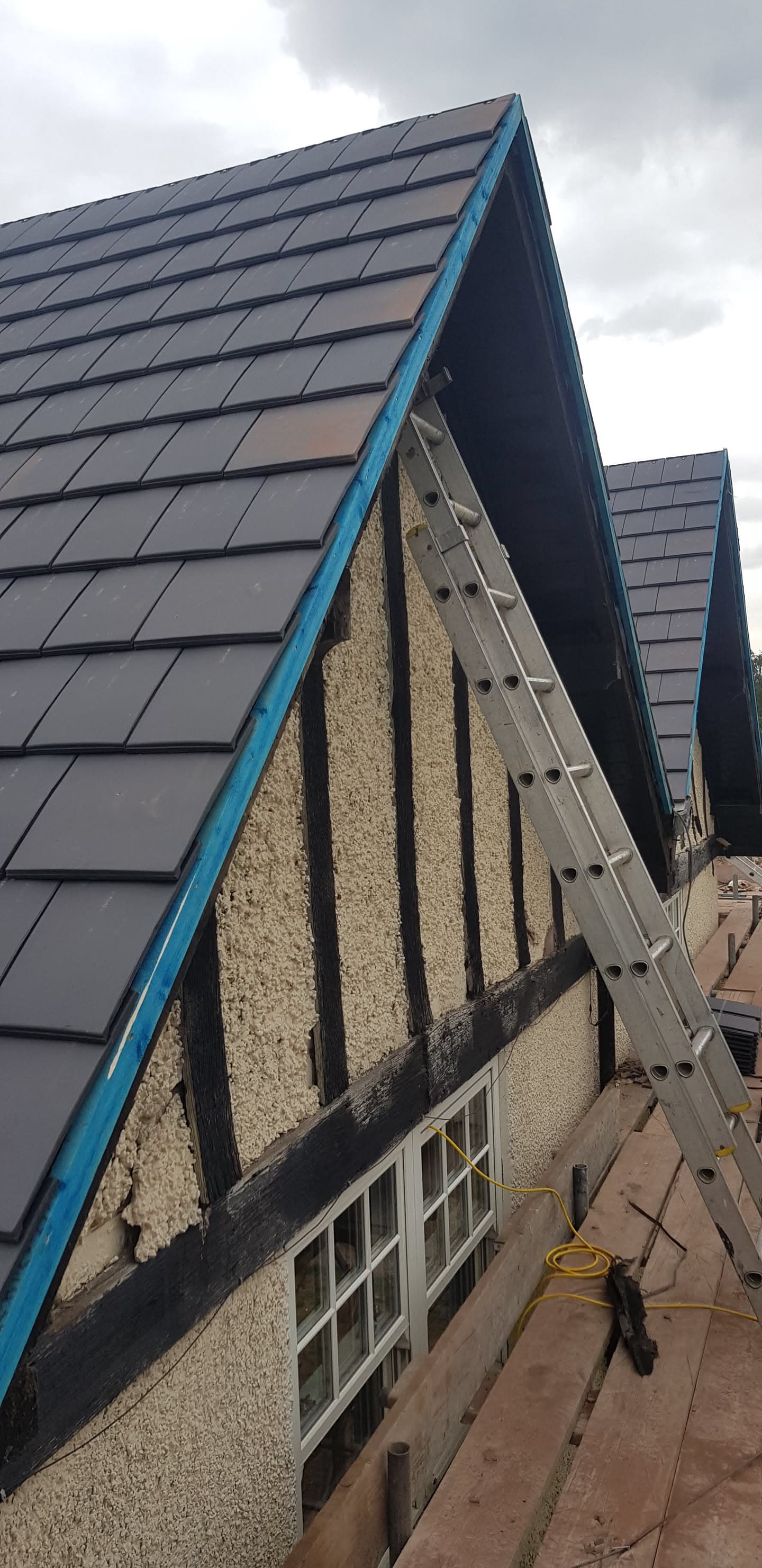 Pitched roof with grey slate tiles and blue fascia boards with ladder against gable end