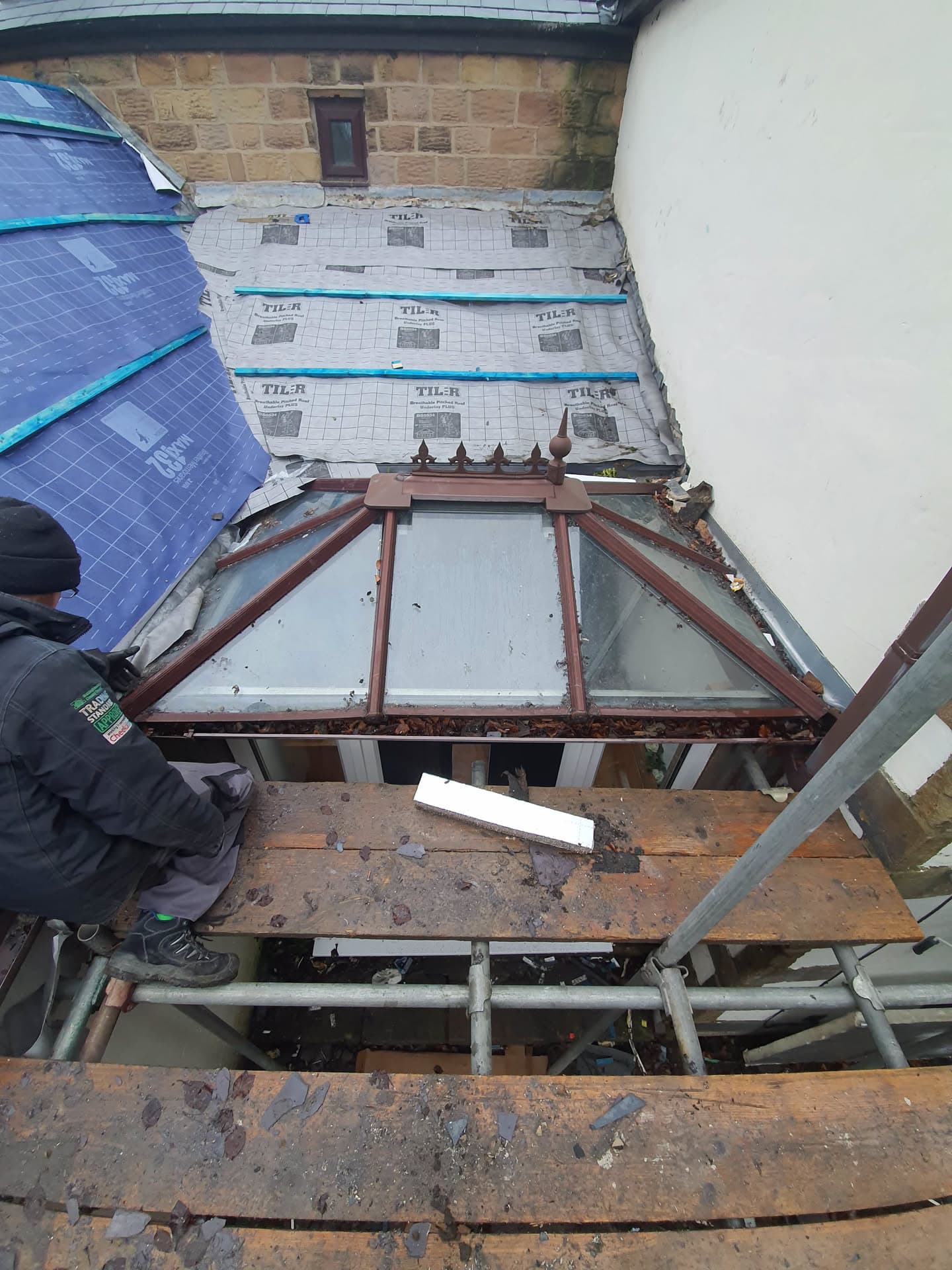Fitter working on pitched roof with blue slate tiles and conservatory roof structure below