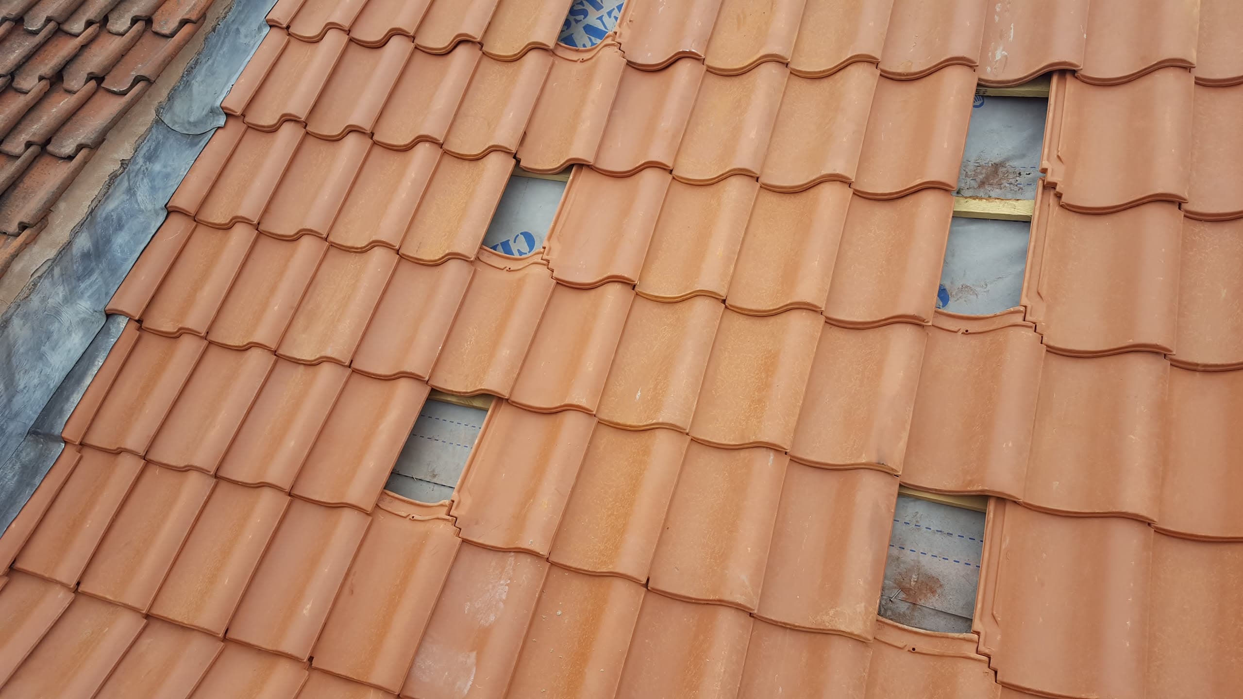 Pitched roof with terracotta concrete tiles being replaced, showing gaps where old tiles removed