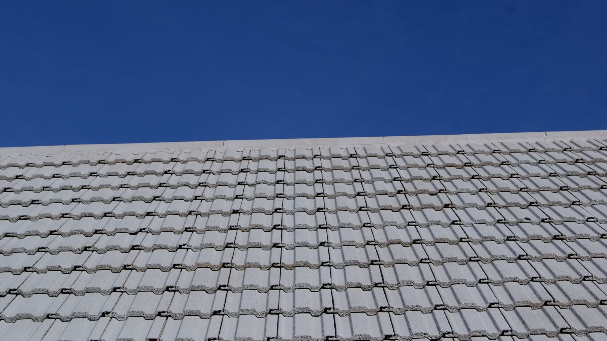 Pitched roof with grey concrete interlocking tiles against clear blue sky