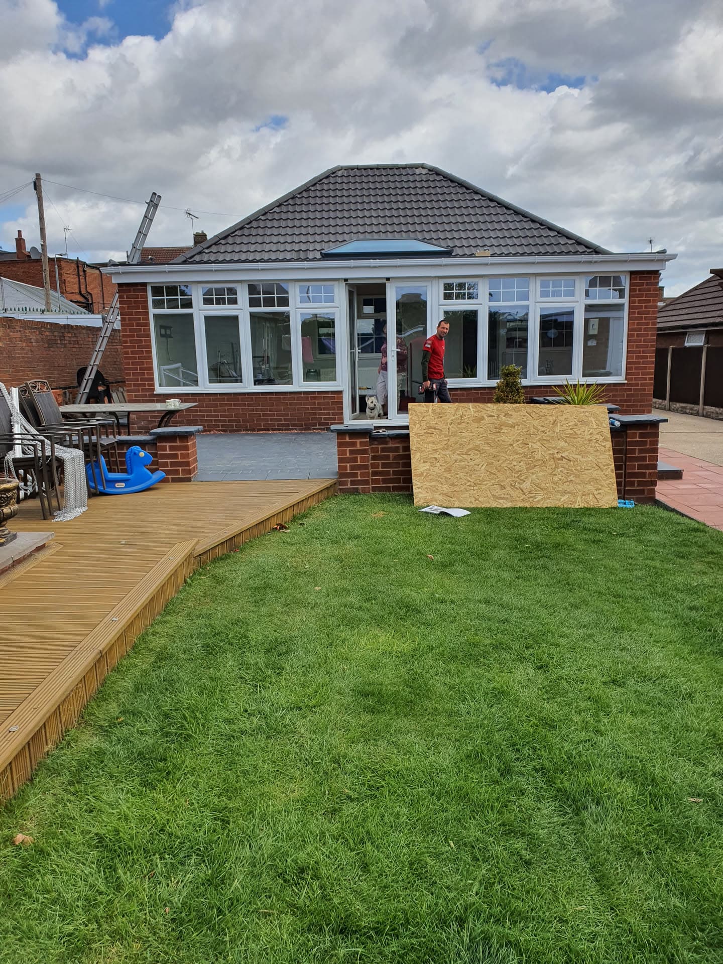 Bungalow with dark grey tiled conservatory roof and white uPVC windows, fitter working on site