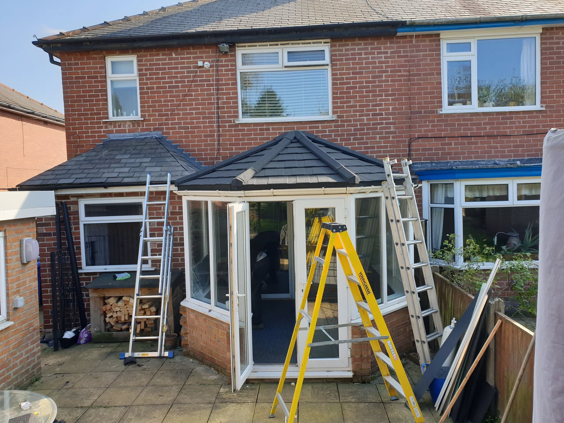 Conservatory roof with dark grey tiles and white fascias, ladders positioned for installation work