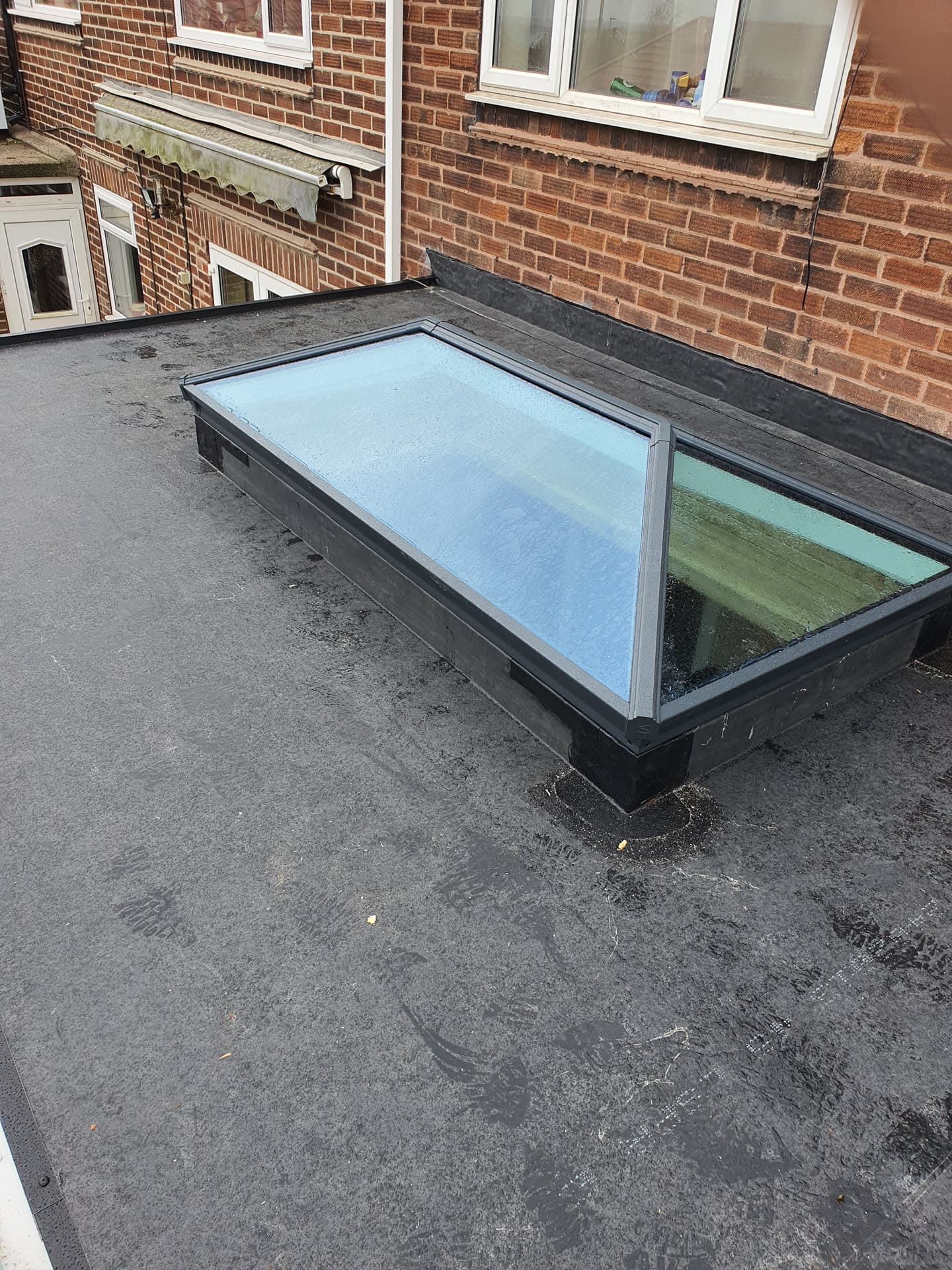 Flat roof with two aluminium-framed roof lanterns on dark felt surface
