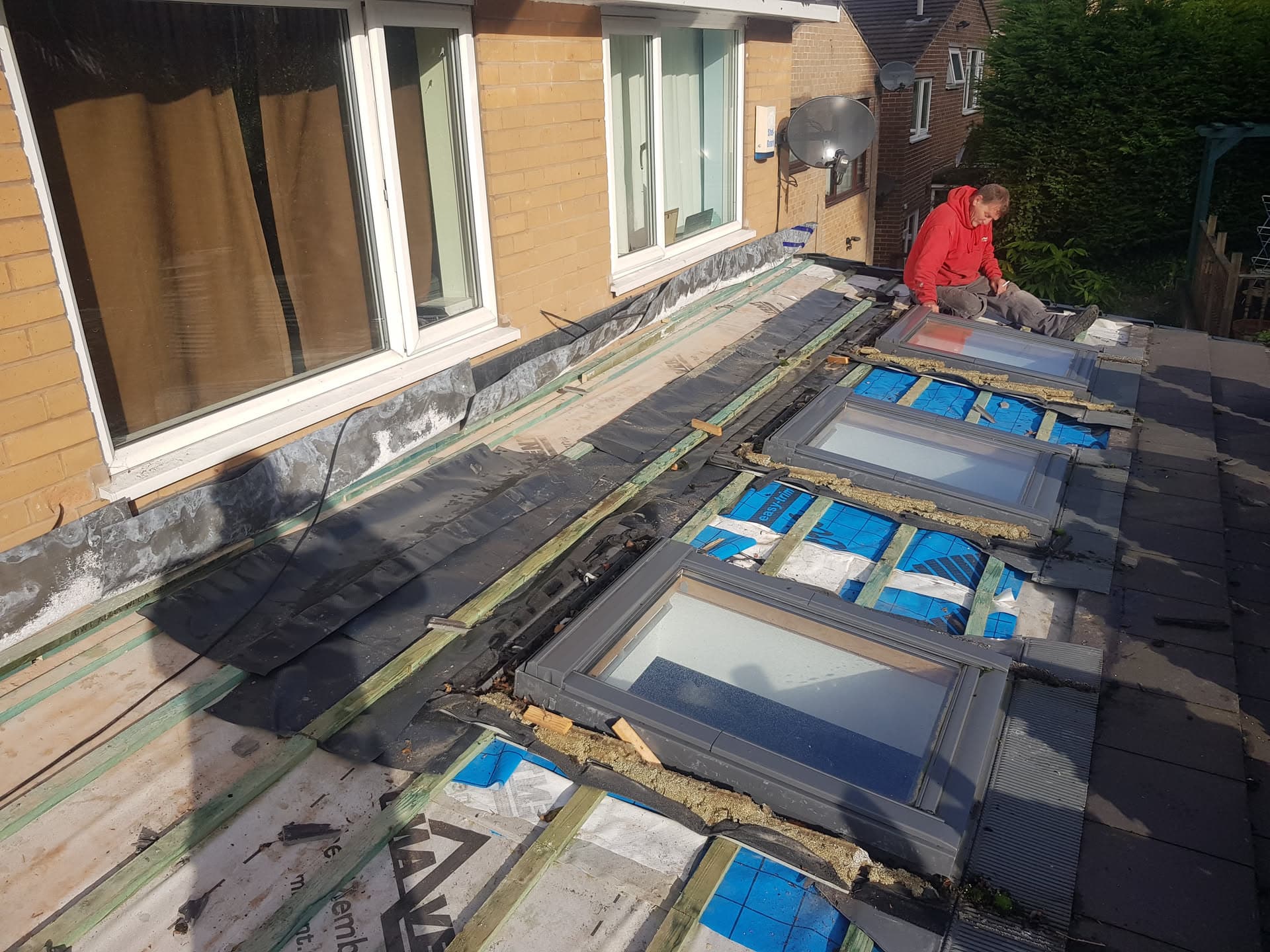 Fitter installing dark grey tiles on conservatory roof with exposed timber framework and skylights
