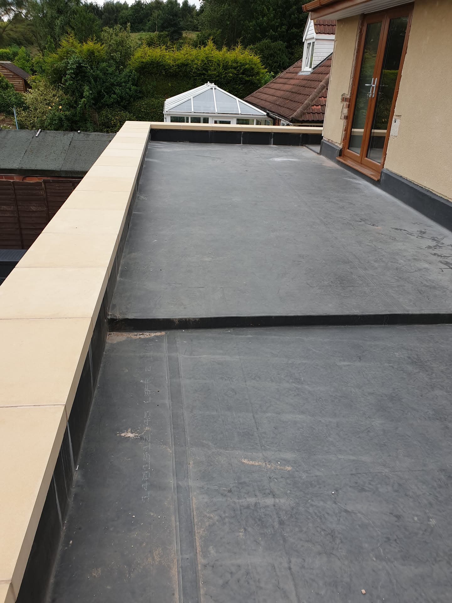 Grey EPDM rubber flat roof with cream fascia trim and conservatory in background