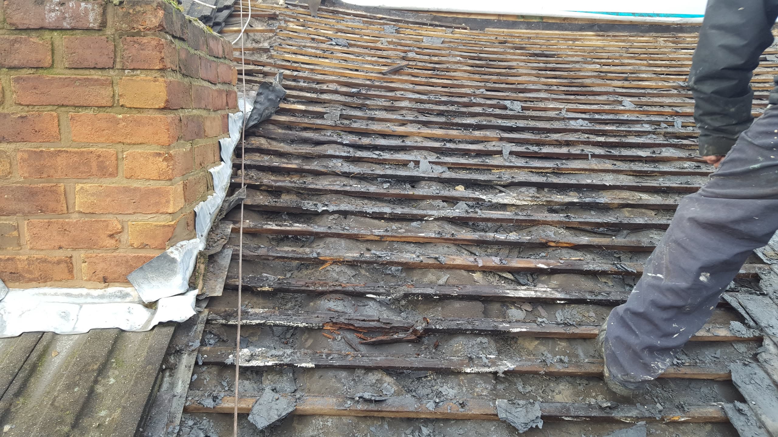 Pitched roof with tiles removed exposing timber battens and lead flashing against brick wall