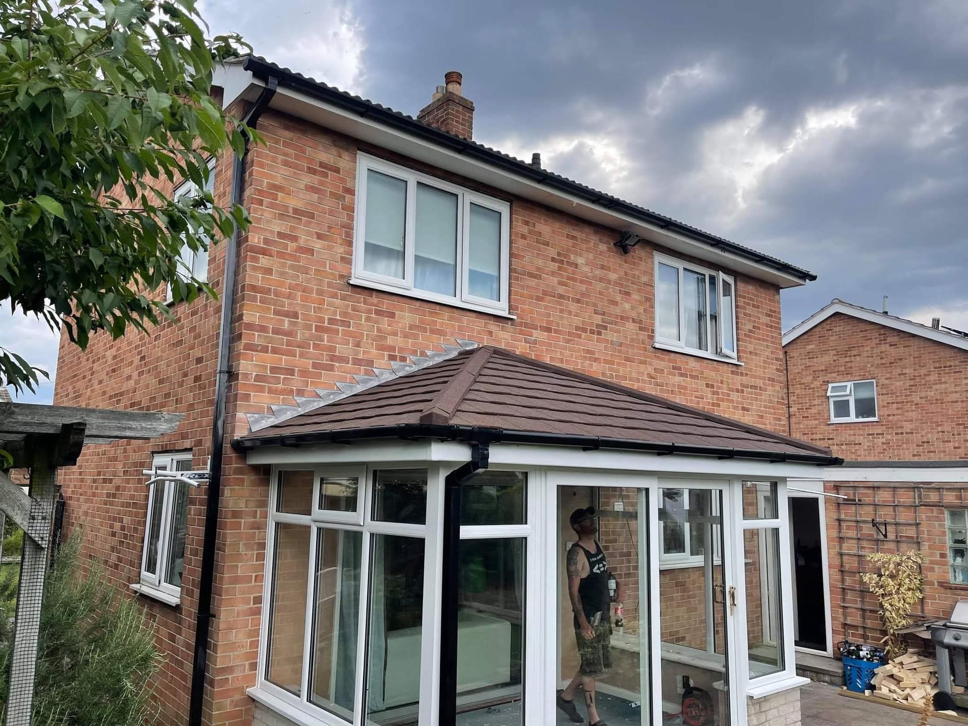Brown tiled conservatory roof on brick house with dark fascias and guttering