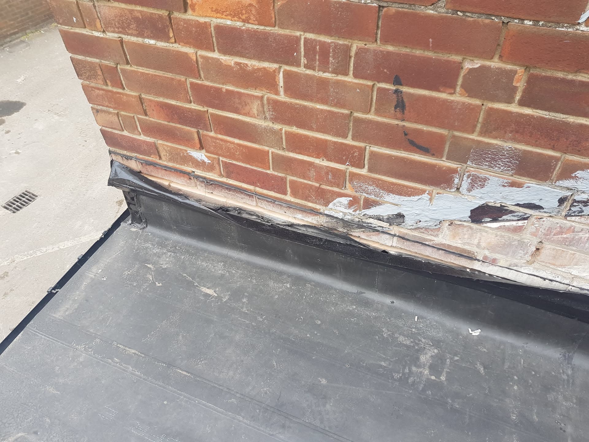 Flat roof with lead flashing against red brick wall showing weathered timber fascia