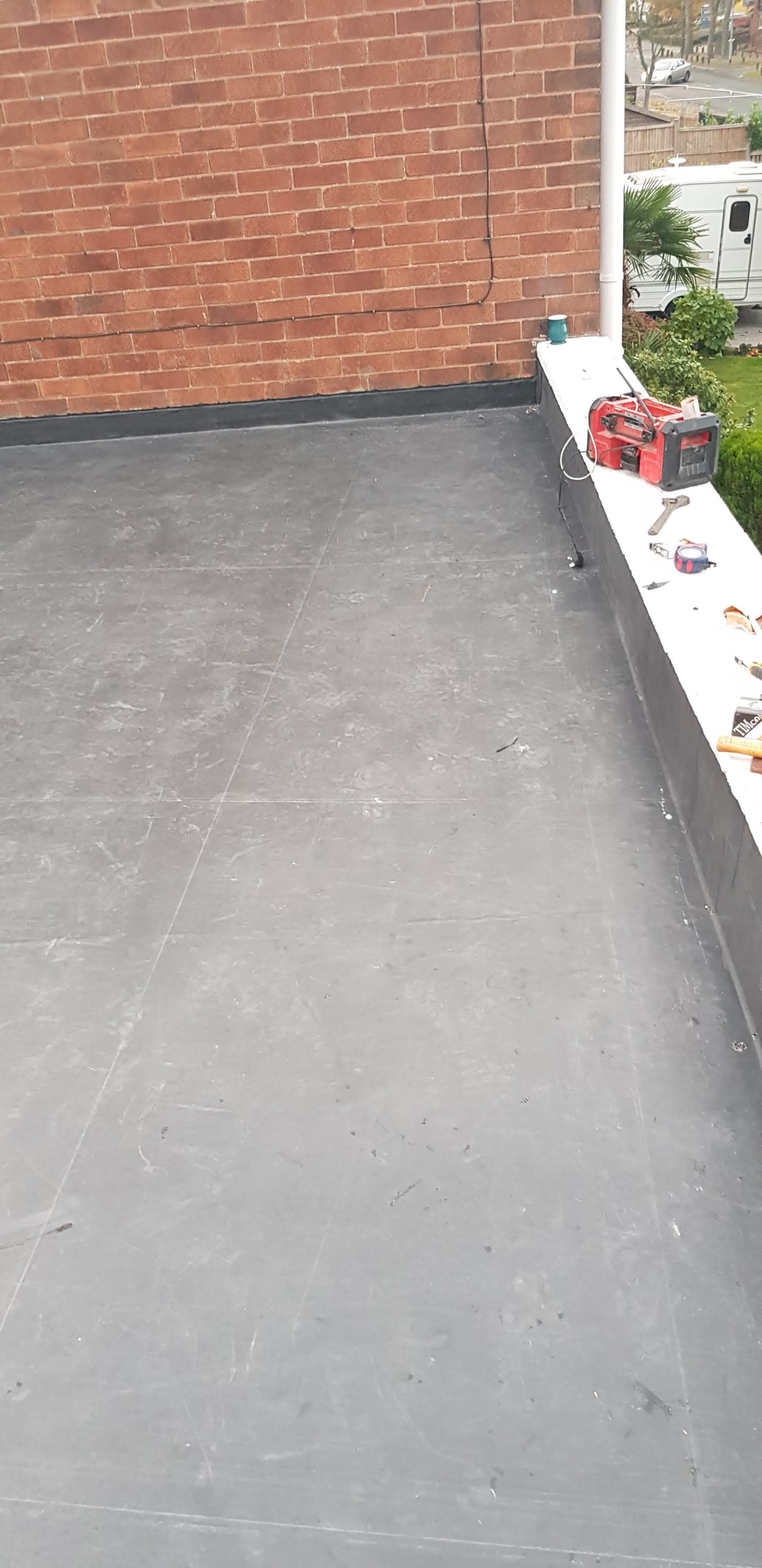 Completed grey EPDM rubber flat roof with upstands against brick wall