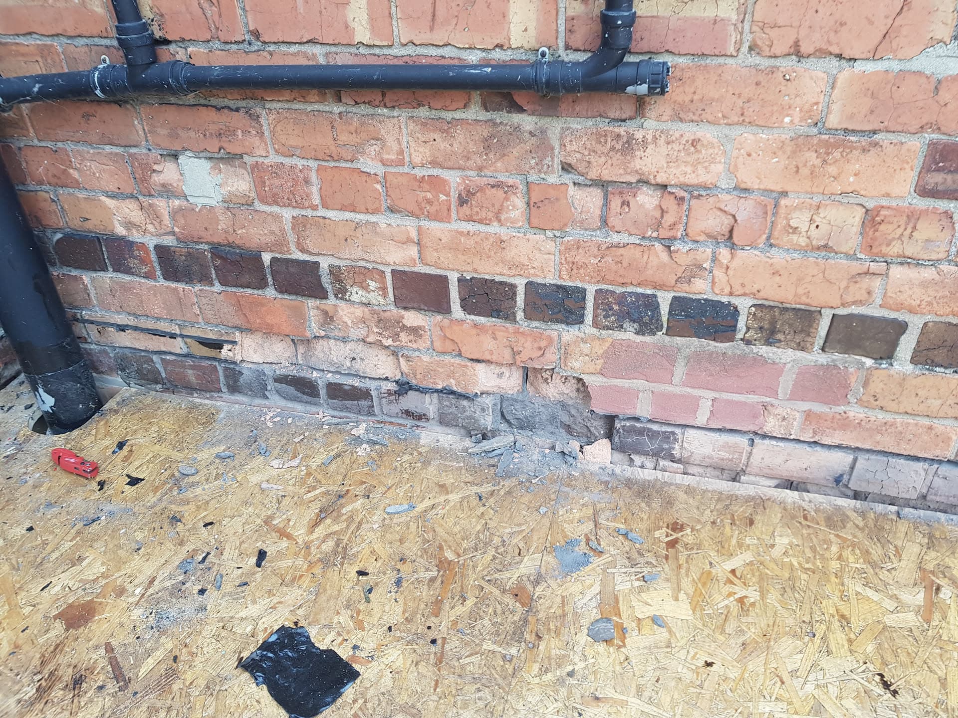 Black plastic pipe fitted to brick wall above OSB board on flat roof