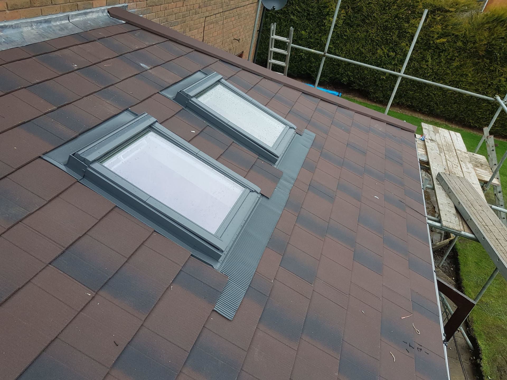 Pitched roof with brown concrete tiles and two grey-framed roof windows with scaffolding alongside