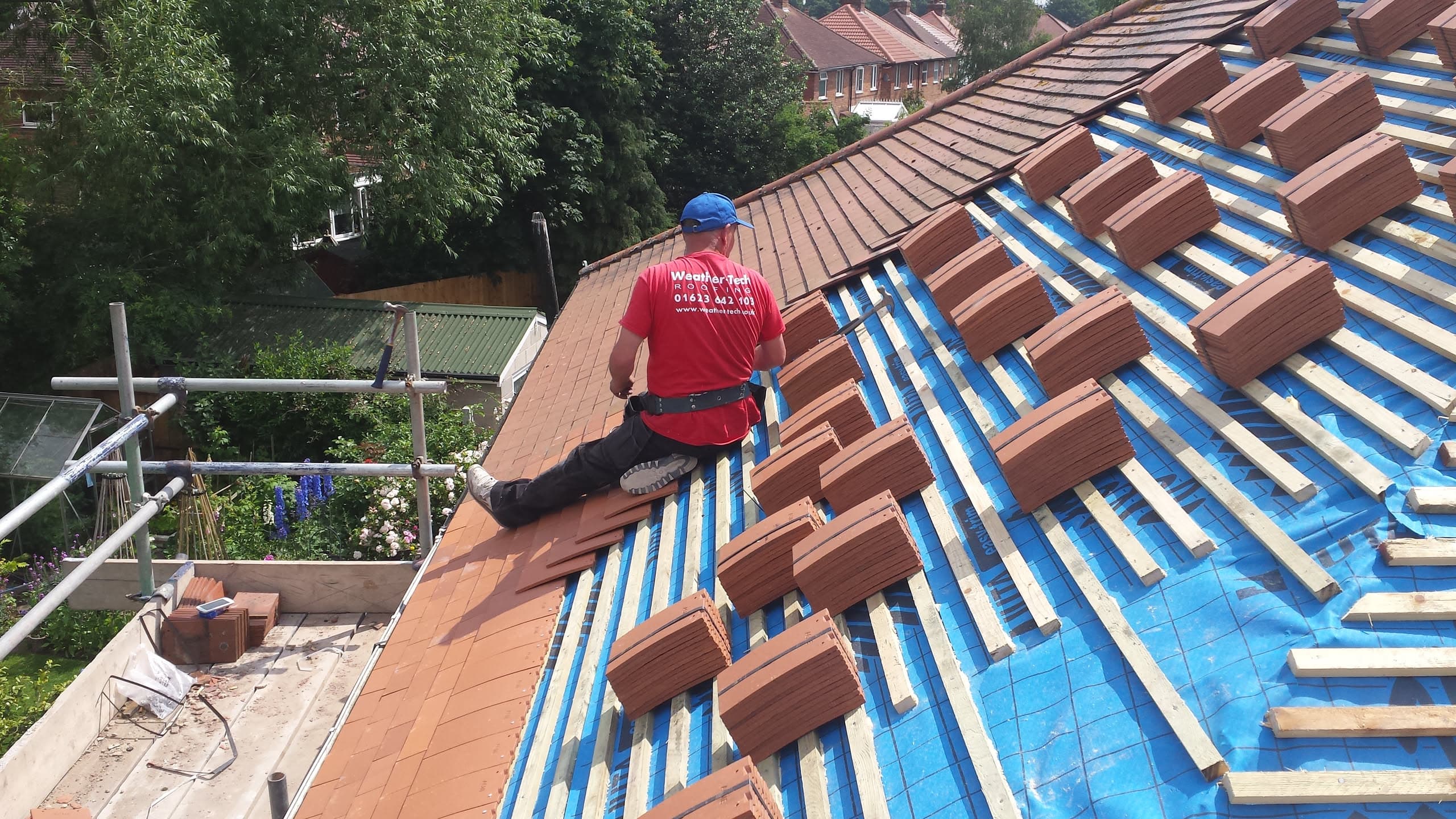 Roofer installing terracotta clay tiles on pitched roof with blue membrane and battens