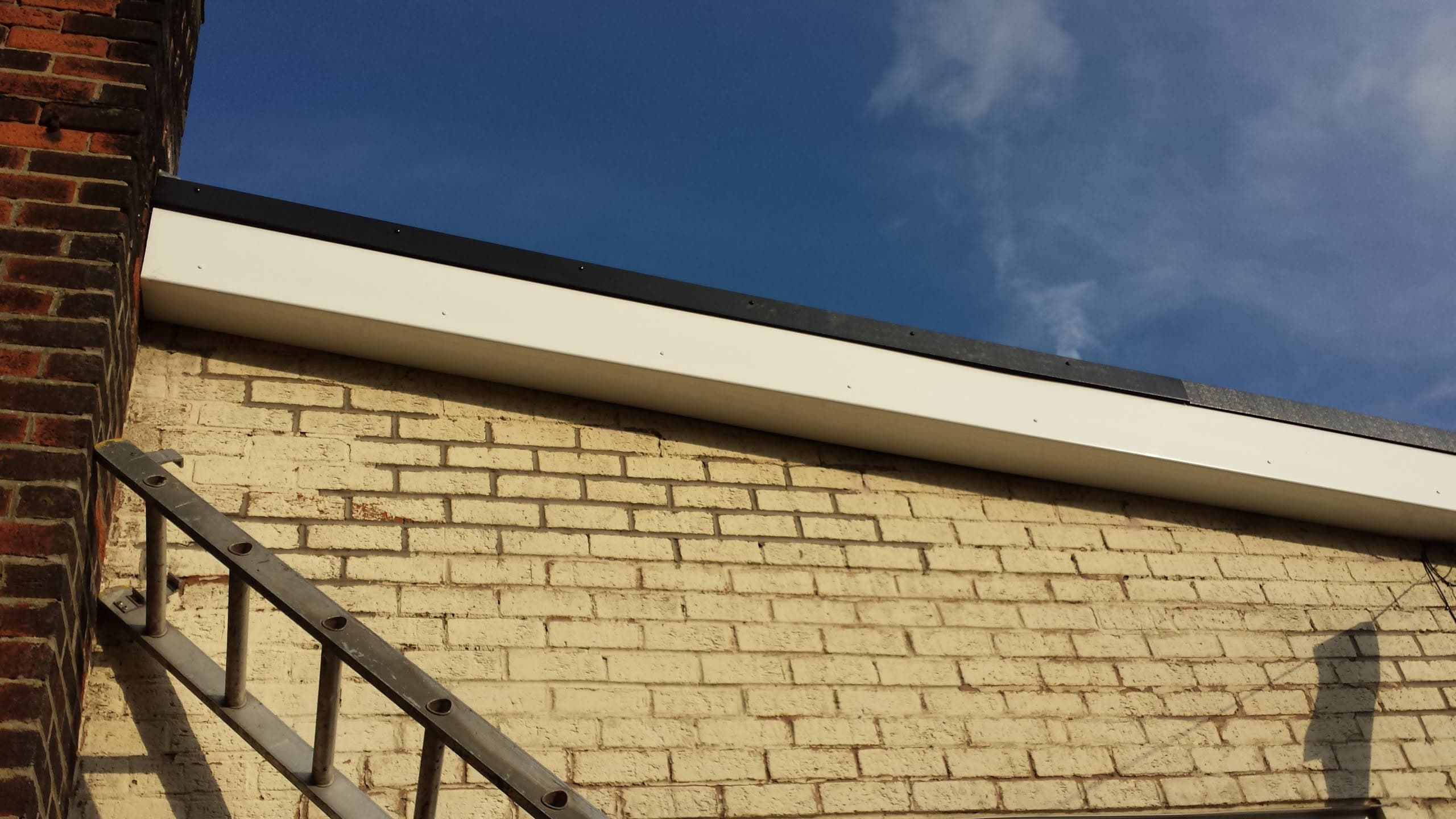 White fascia board and dark grey flat roof edge on cream brick building