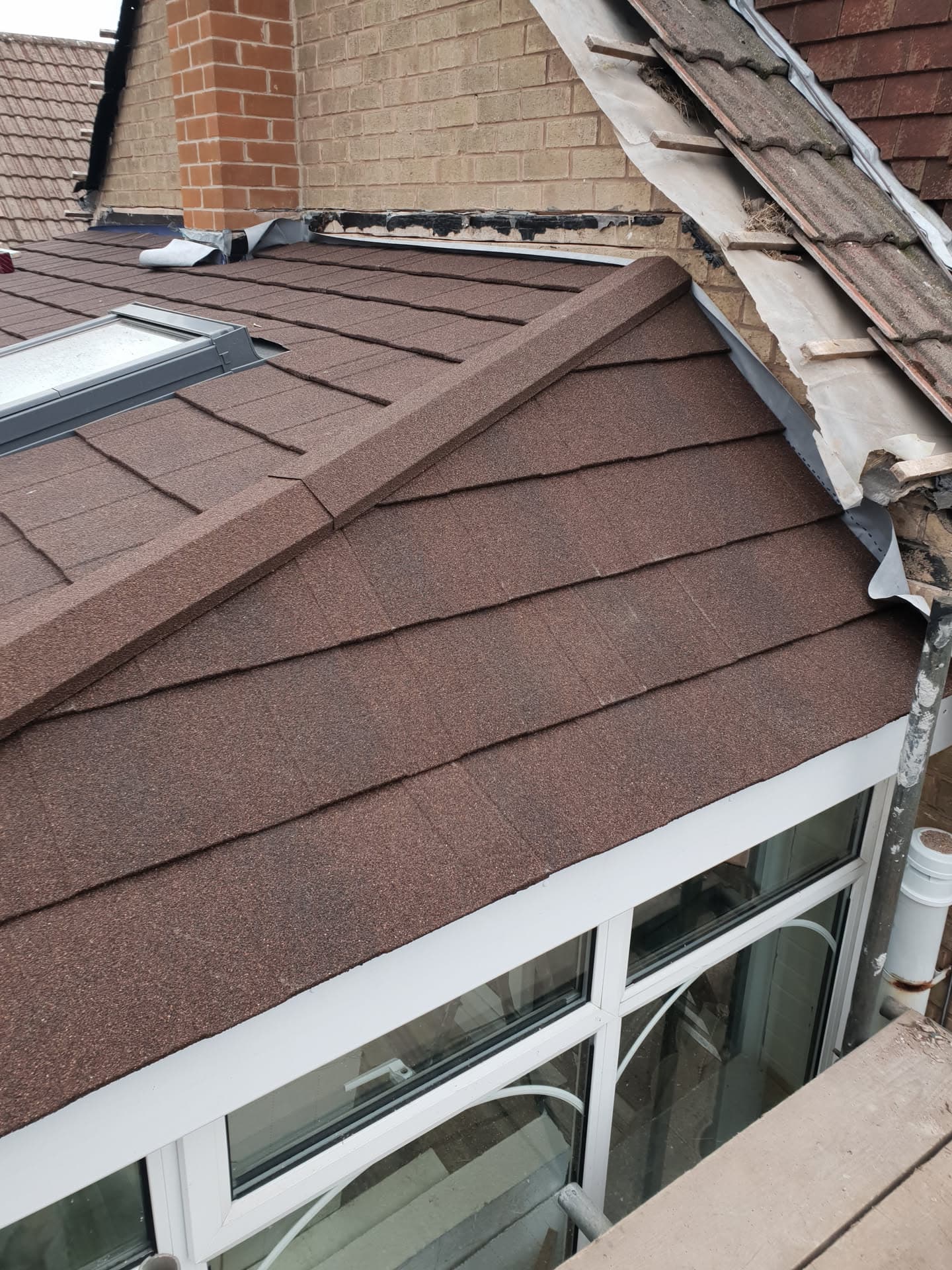 Brown flat roof with felt covering on pitched extension, chimney and velux window visible