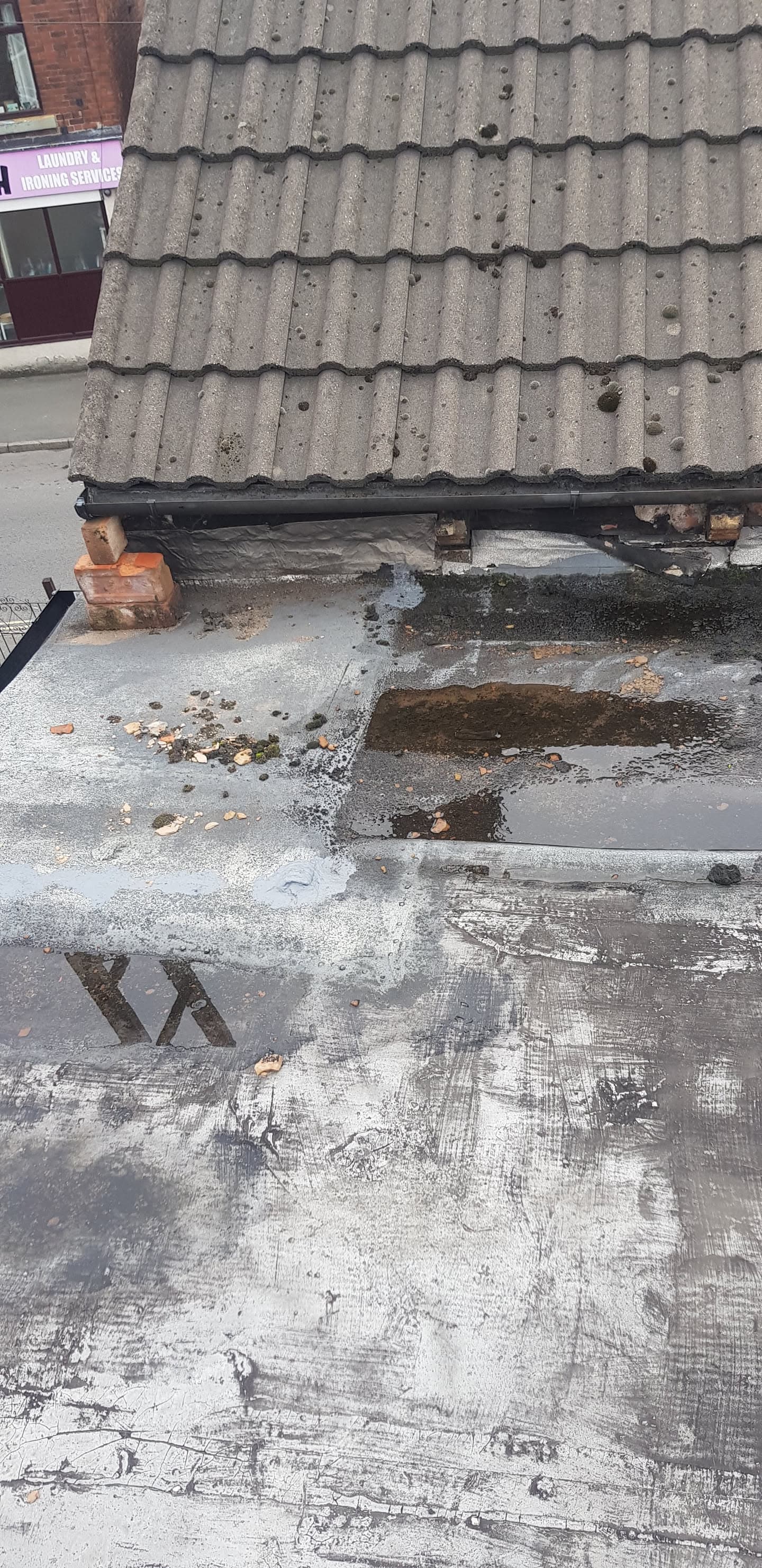 Weathered flat roof with damaged surface and grey concrete tiled pitched roof above