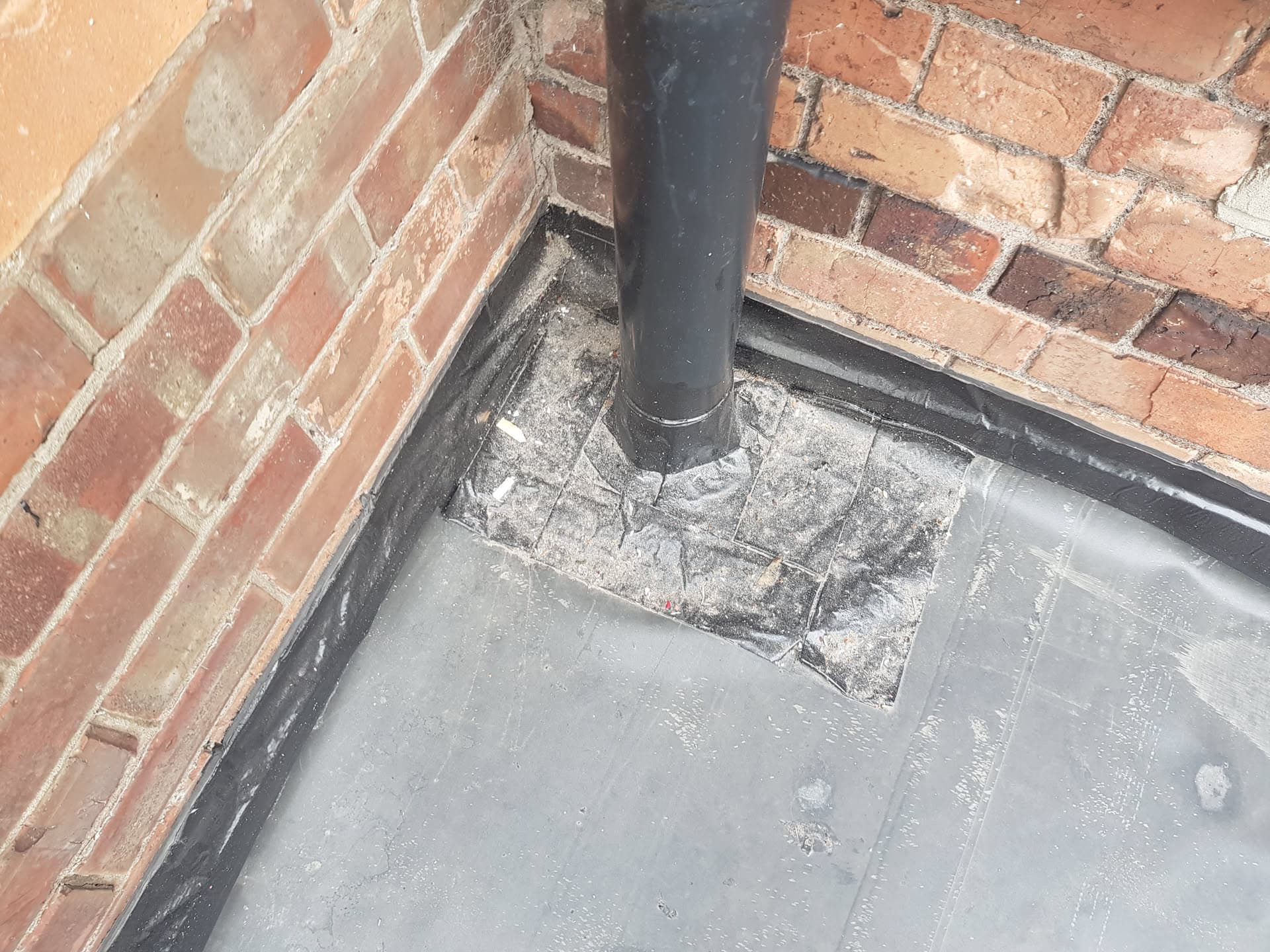 Grey flat roof with soil pipe flashing detail against red brick wall