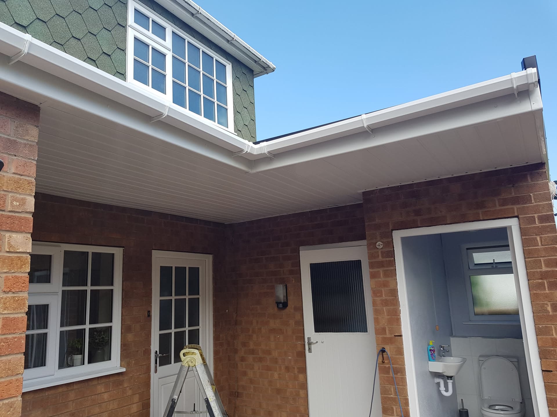 White fascias, soffits and guttering installed on brick property with green tiled pitched roof