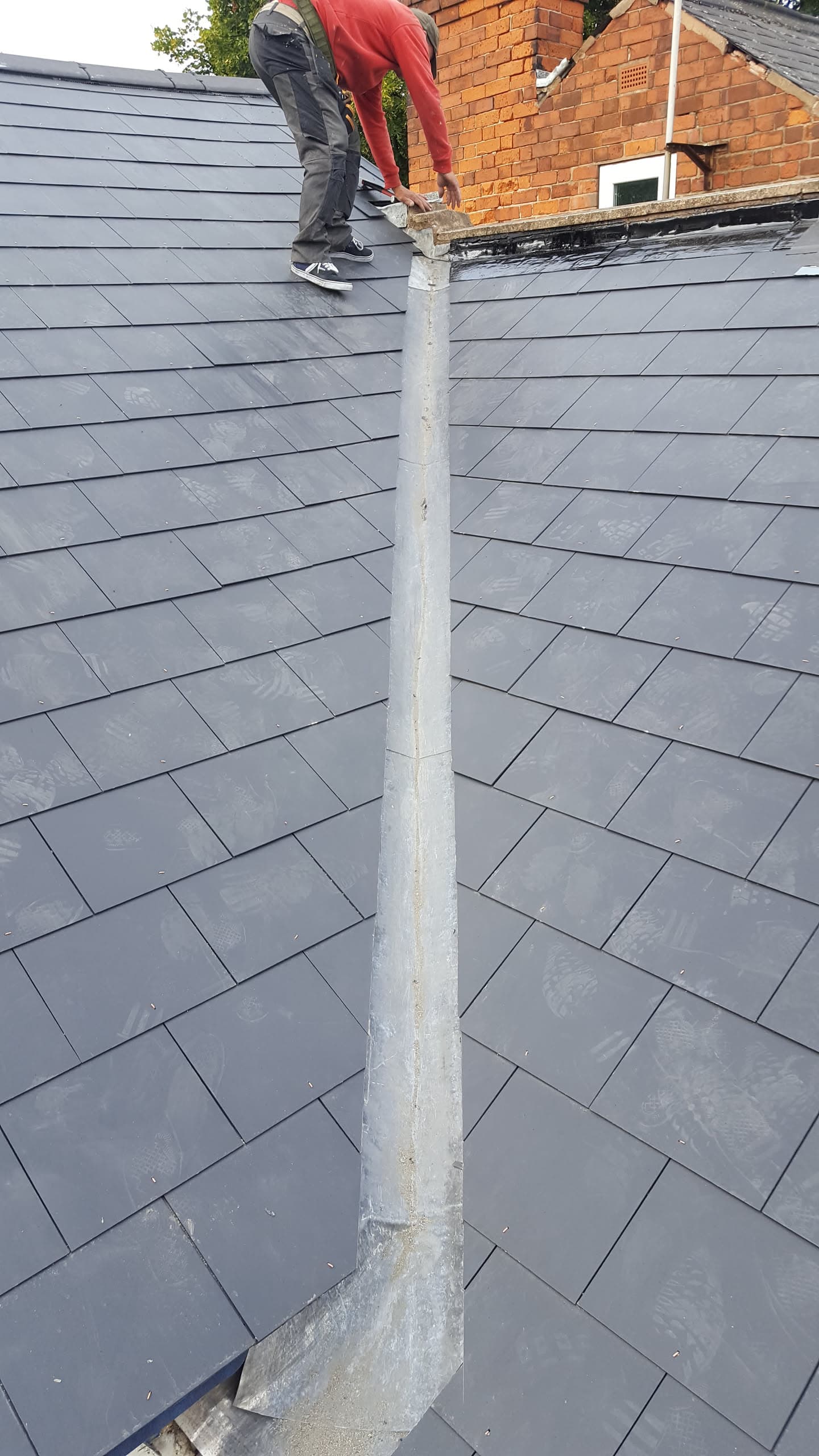 Fitter working on grey slate pitched roof with lead ridge flashing