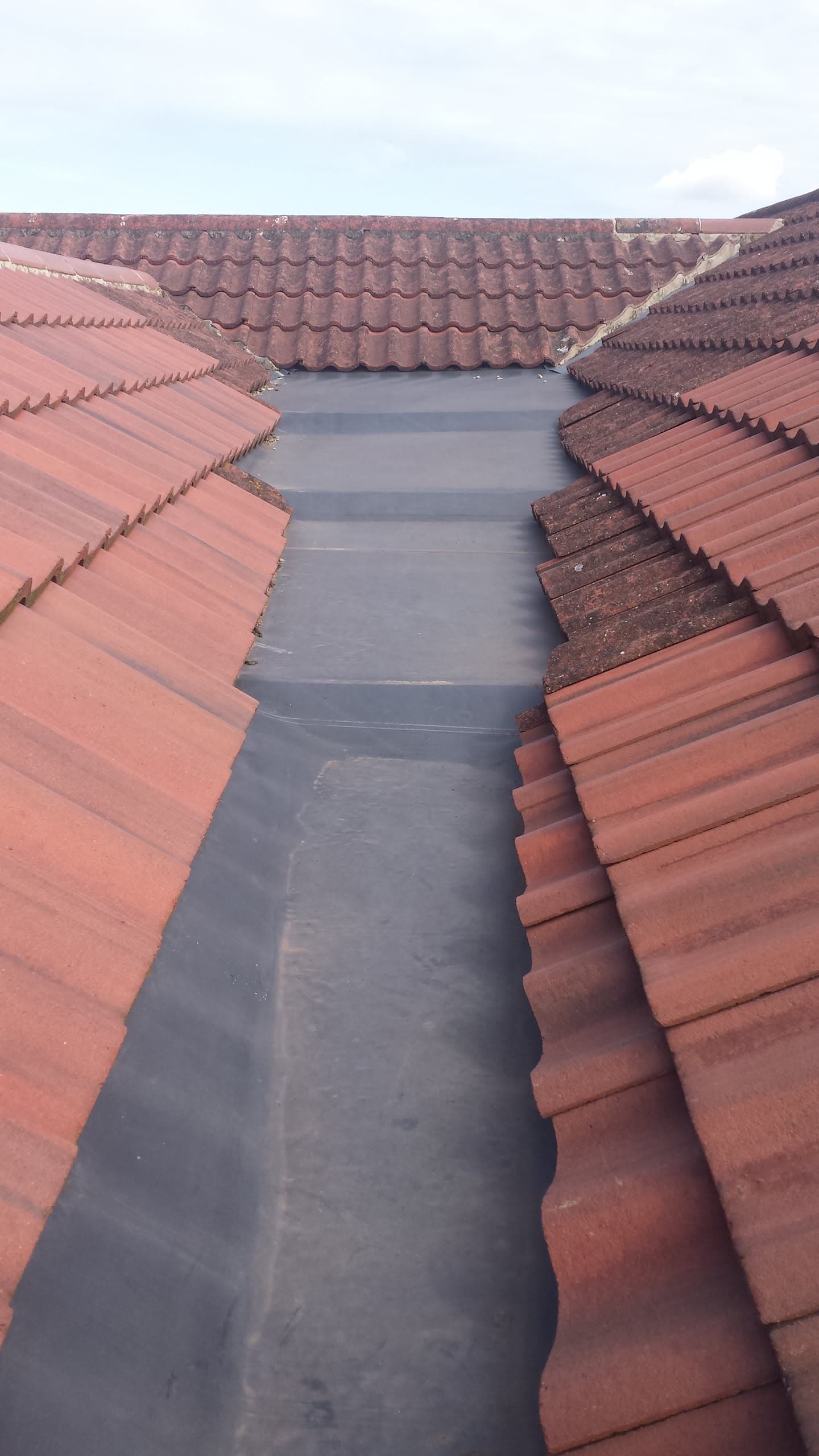 Flat roof valley with grey felt between terracotta concrete tiled pitched roof sections
