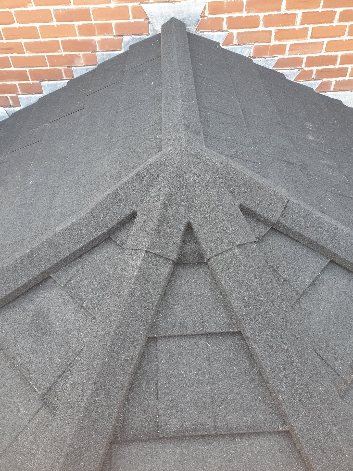 Grey tiled pitched roof valley and ridge detail against brick chimney