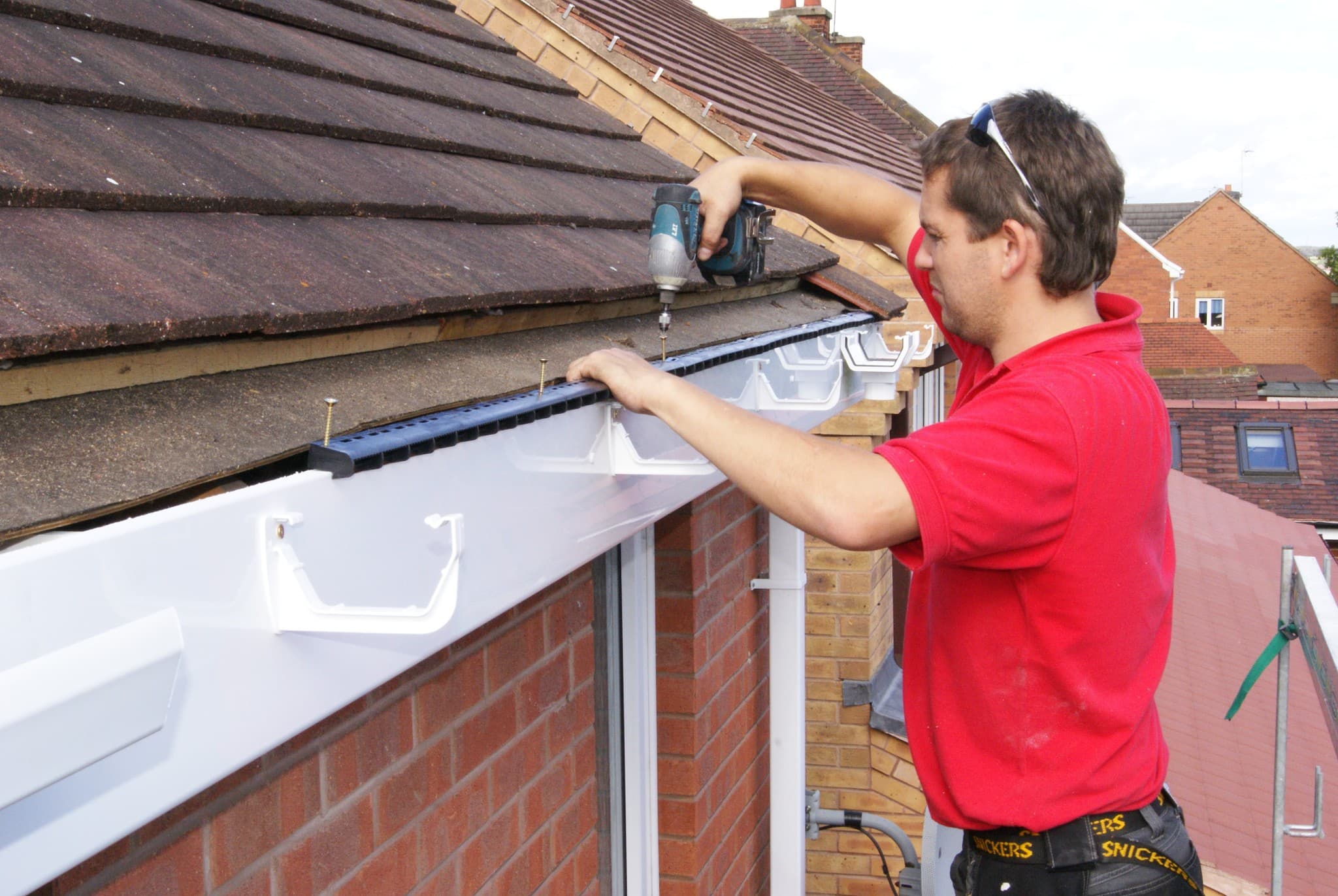 Fitter installing black guttering to pitched tiled roof with power drill