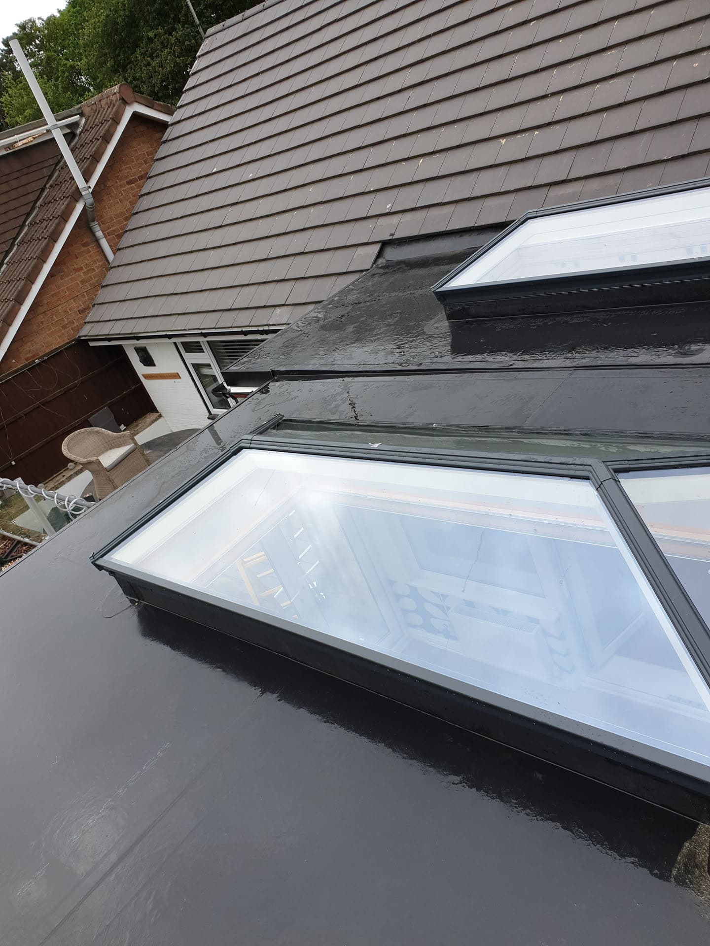Flat roof with three glazed rooflights and brown tiled pitched roof behind